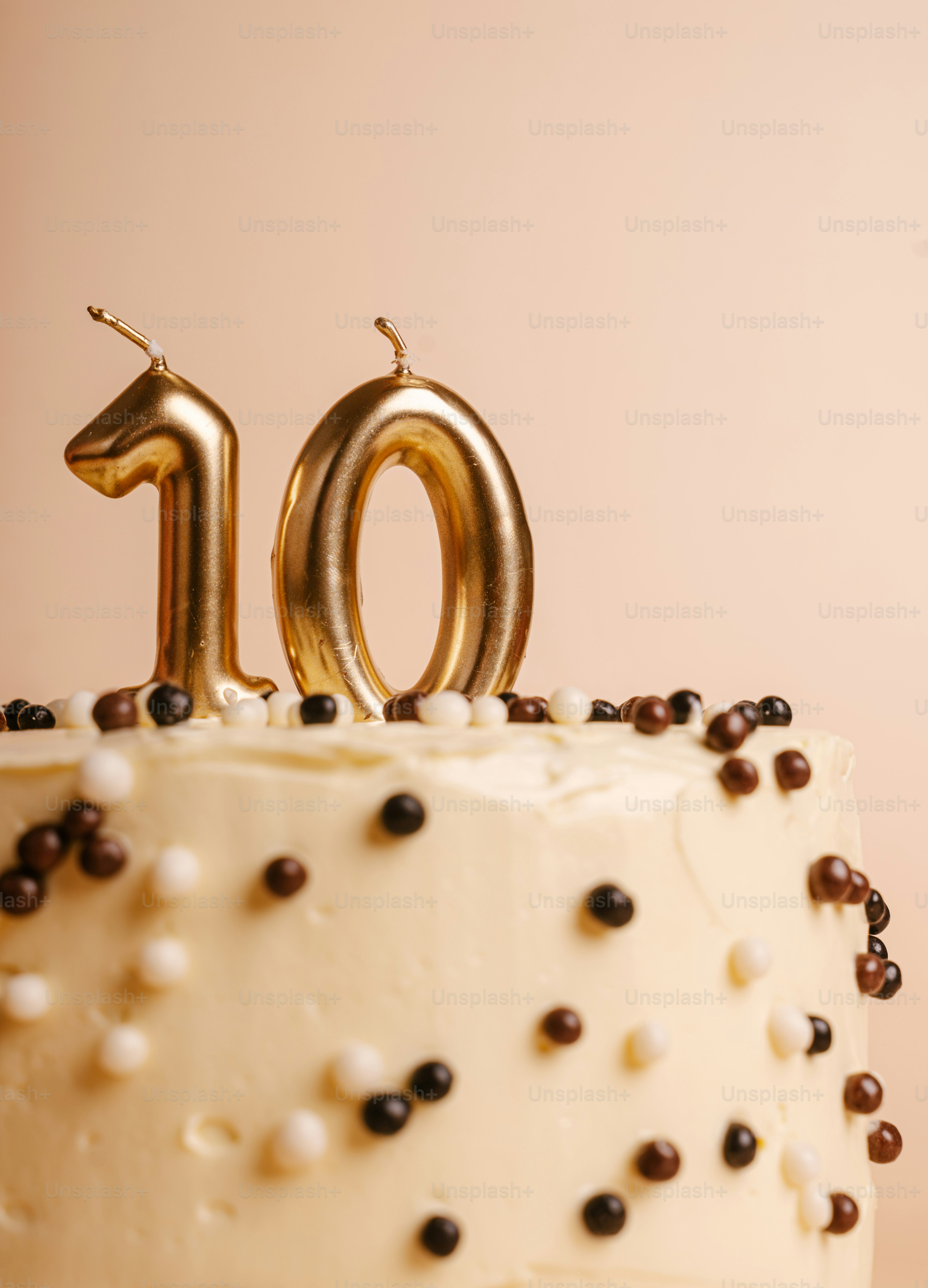 A cake with white frosting and chocolate pearls topped with gold number candles