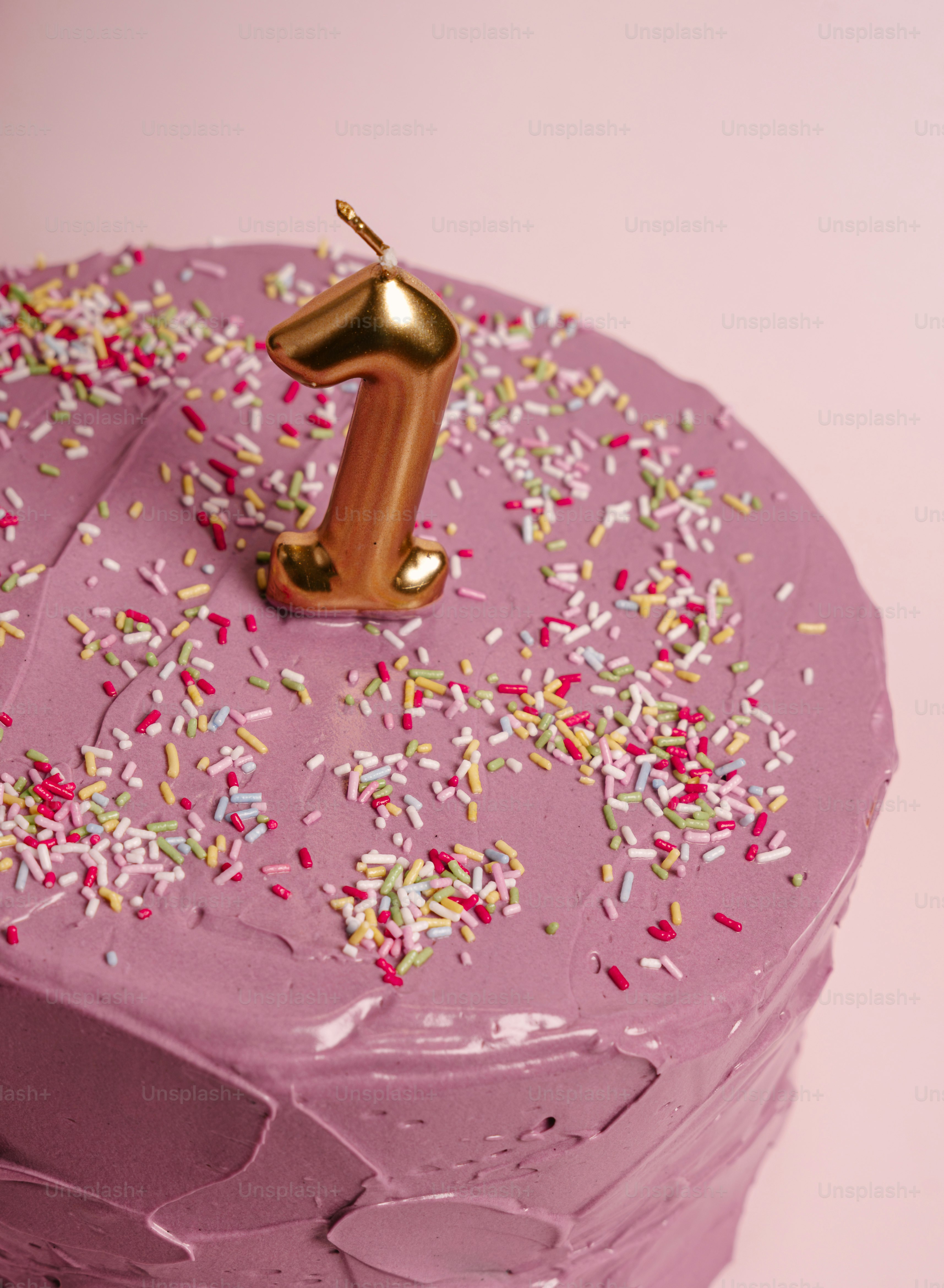 A purple frosted cake with colorful sprinkles and a gold number one candle