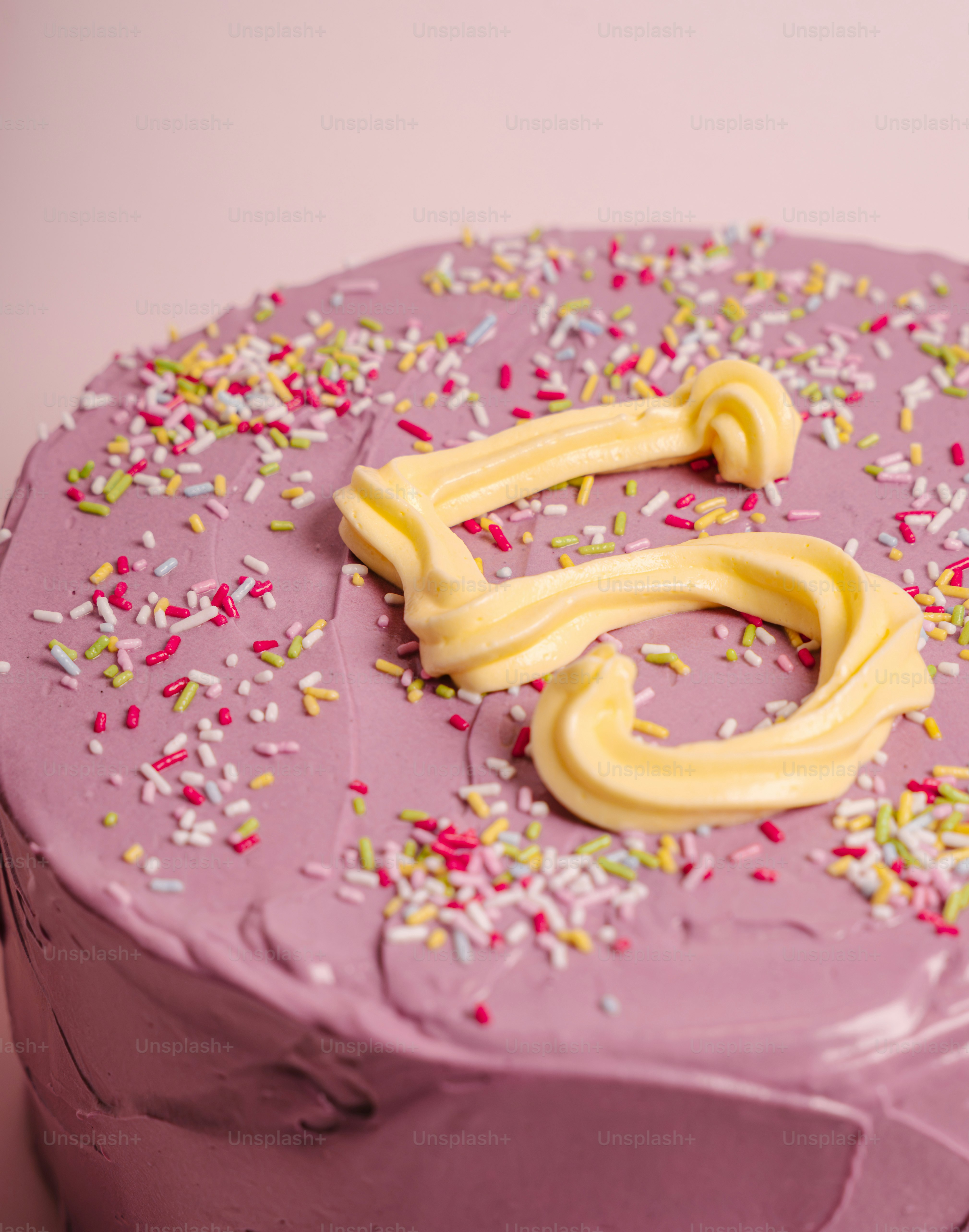 A purple frosted cake with yellow icing number five and colorful sprinkles