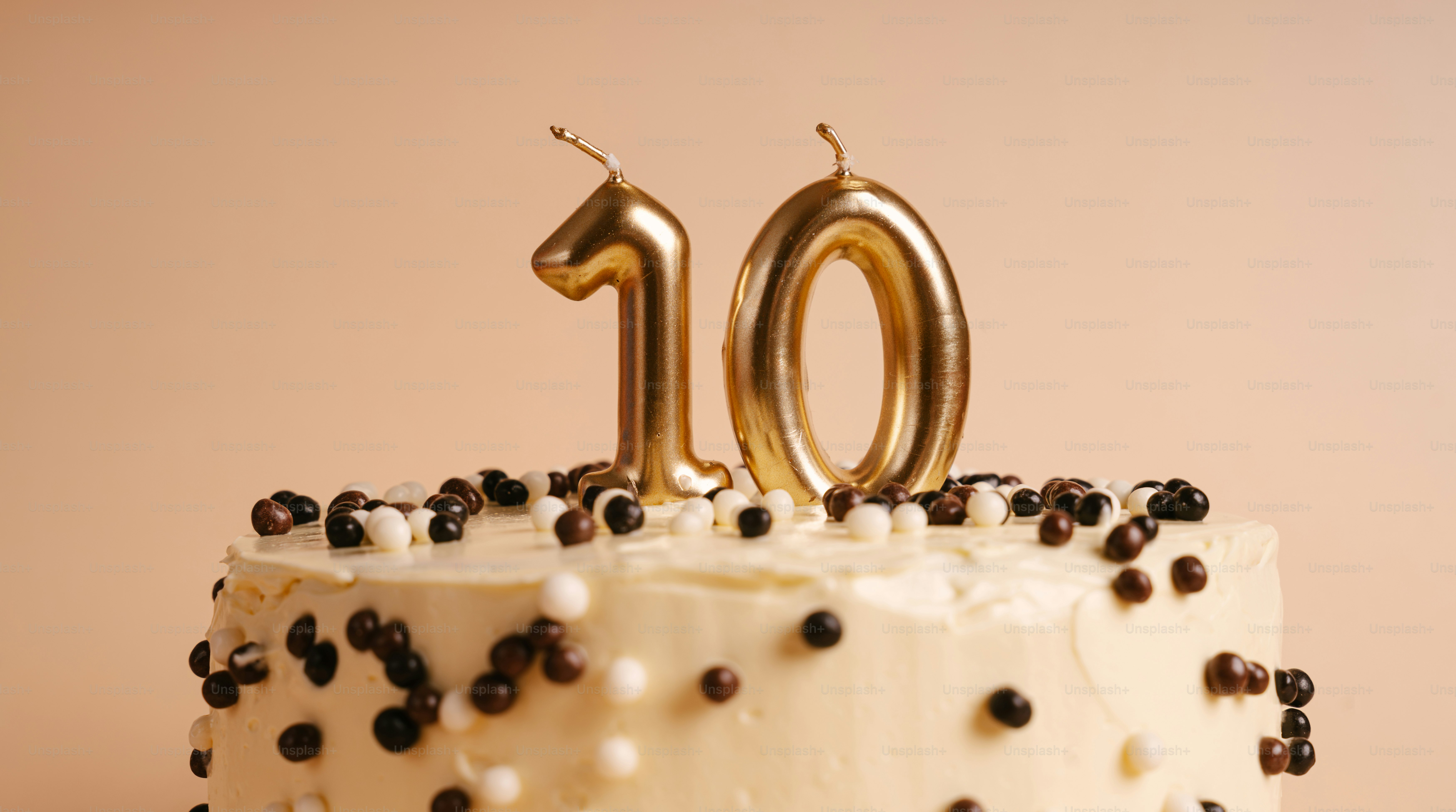 A cake with white frosting and small chocolate balls topped with gold number ten candles