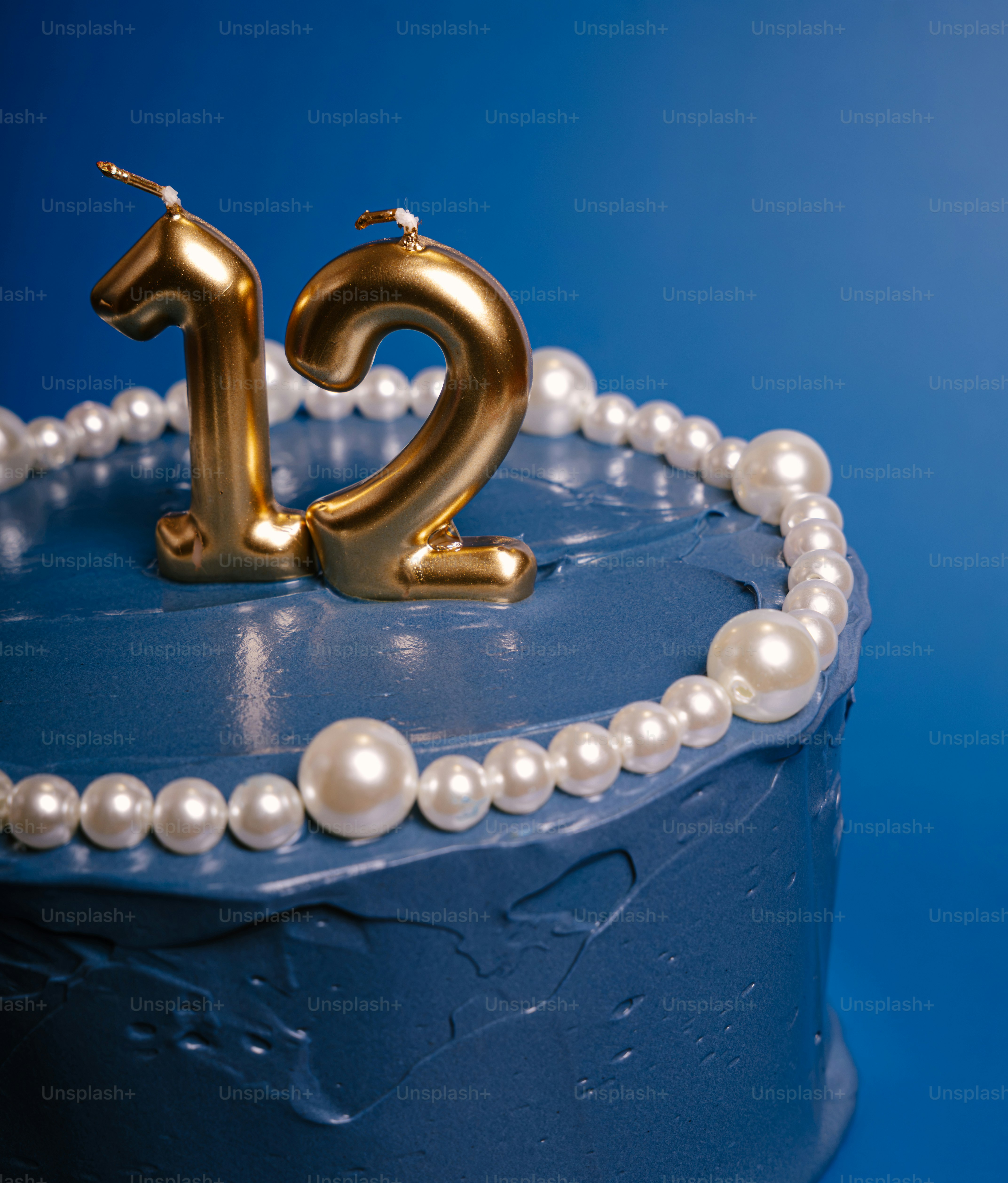A blue cake with gold number twelve candles and a pearl border