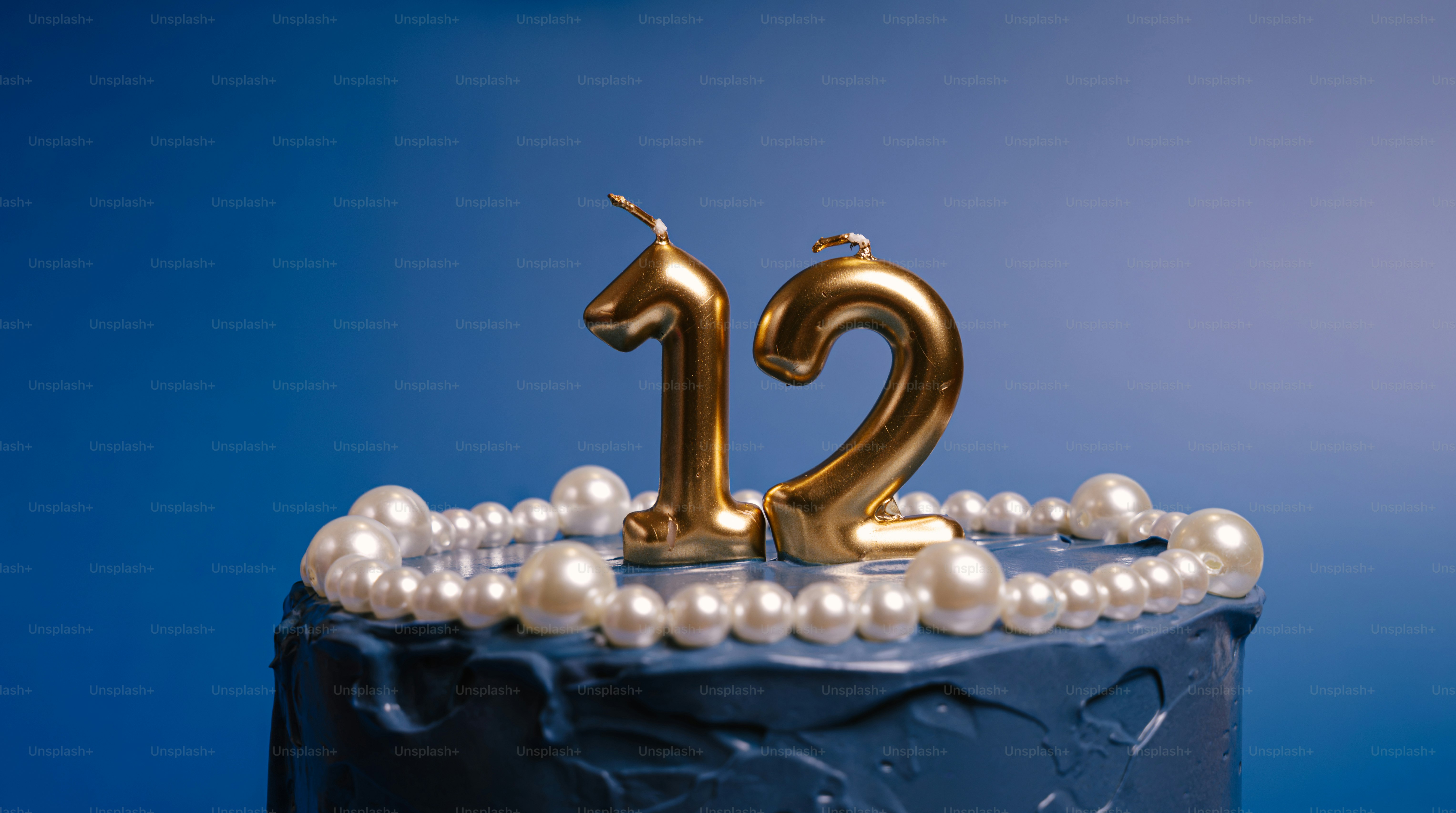 Gold number twelve candles on a blue cake decorated with white pearls