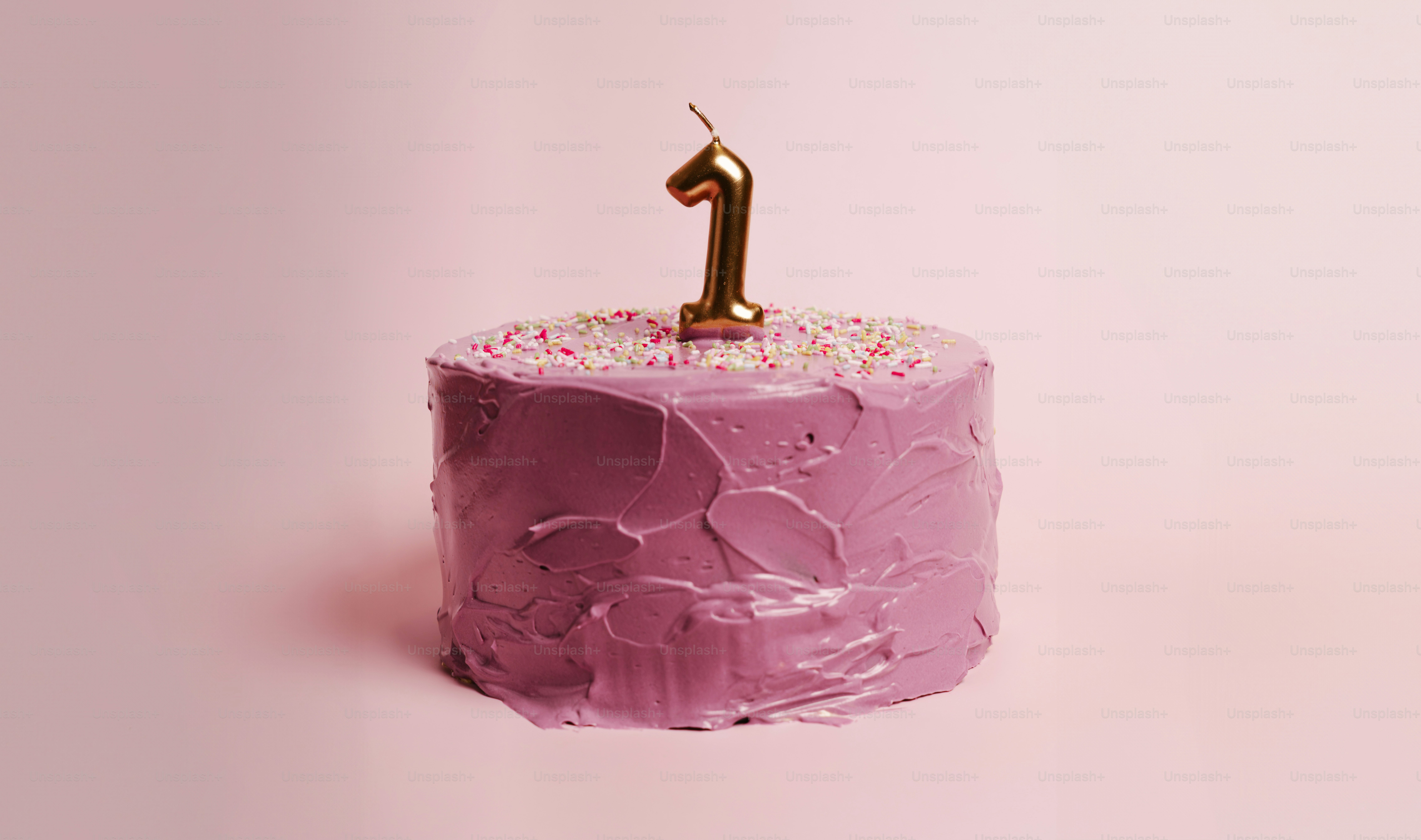 A small purple frosted cake with a gold number one candle on top