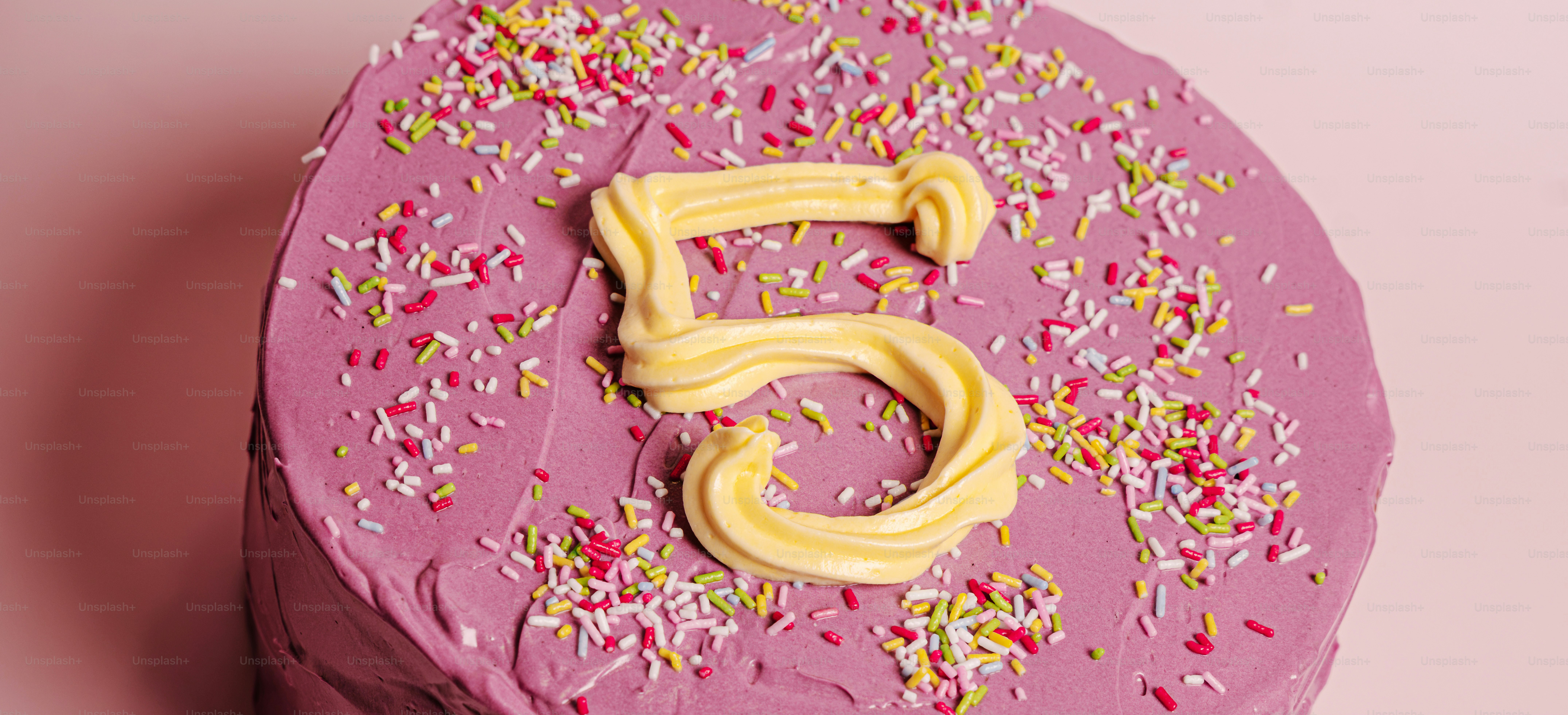 A round cake with purple frosting, colorful sprinkles, and a yellow number five