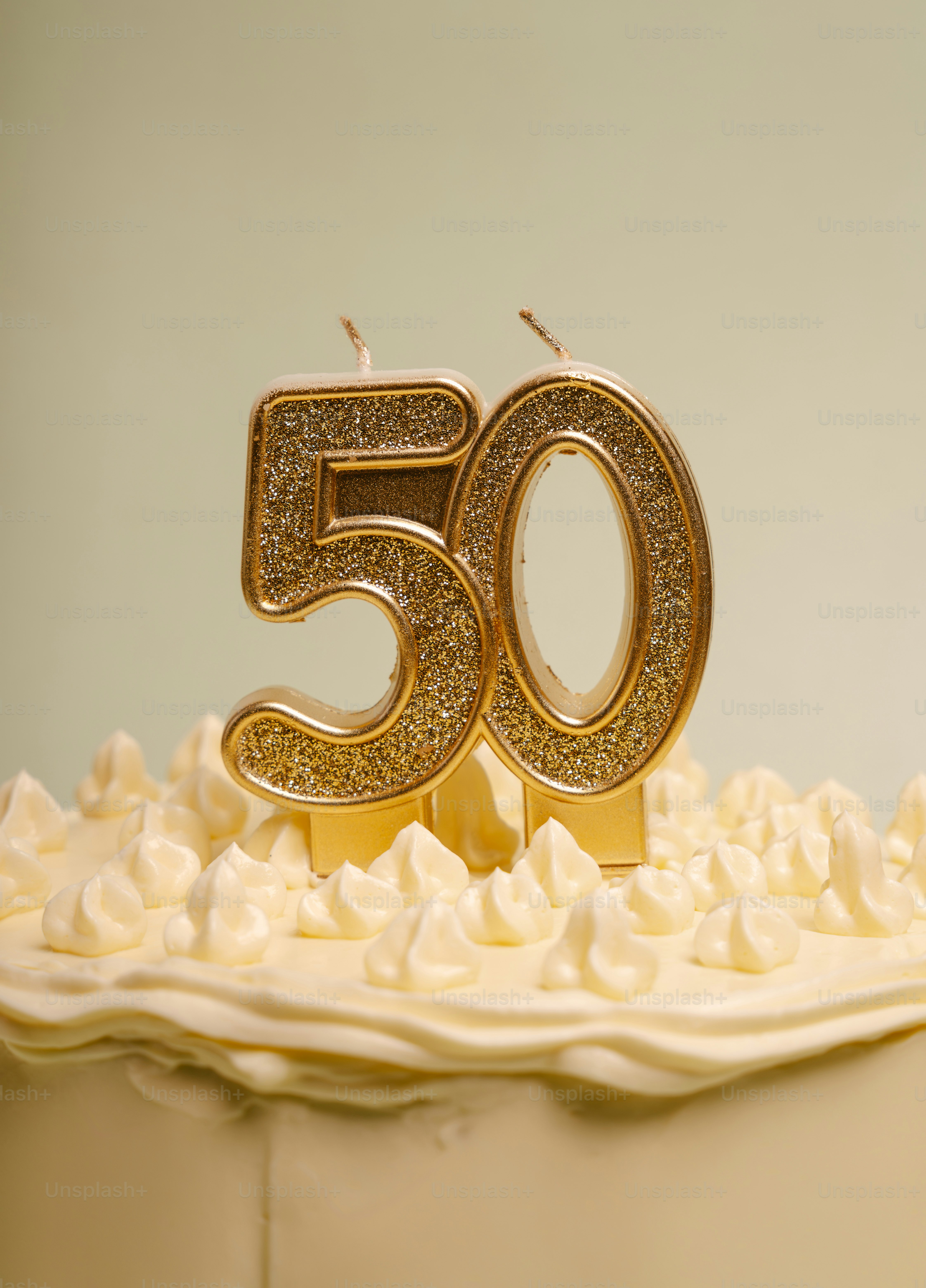 Gold glitter number fifty candles on a white frosted cake