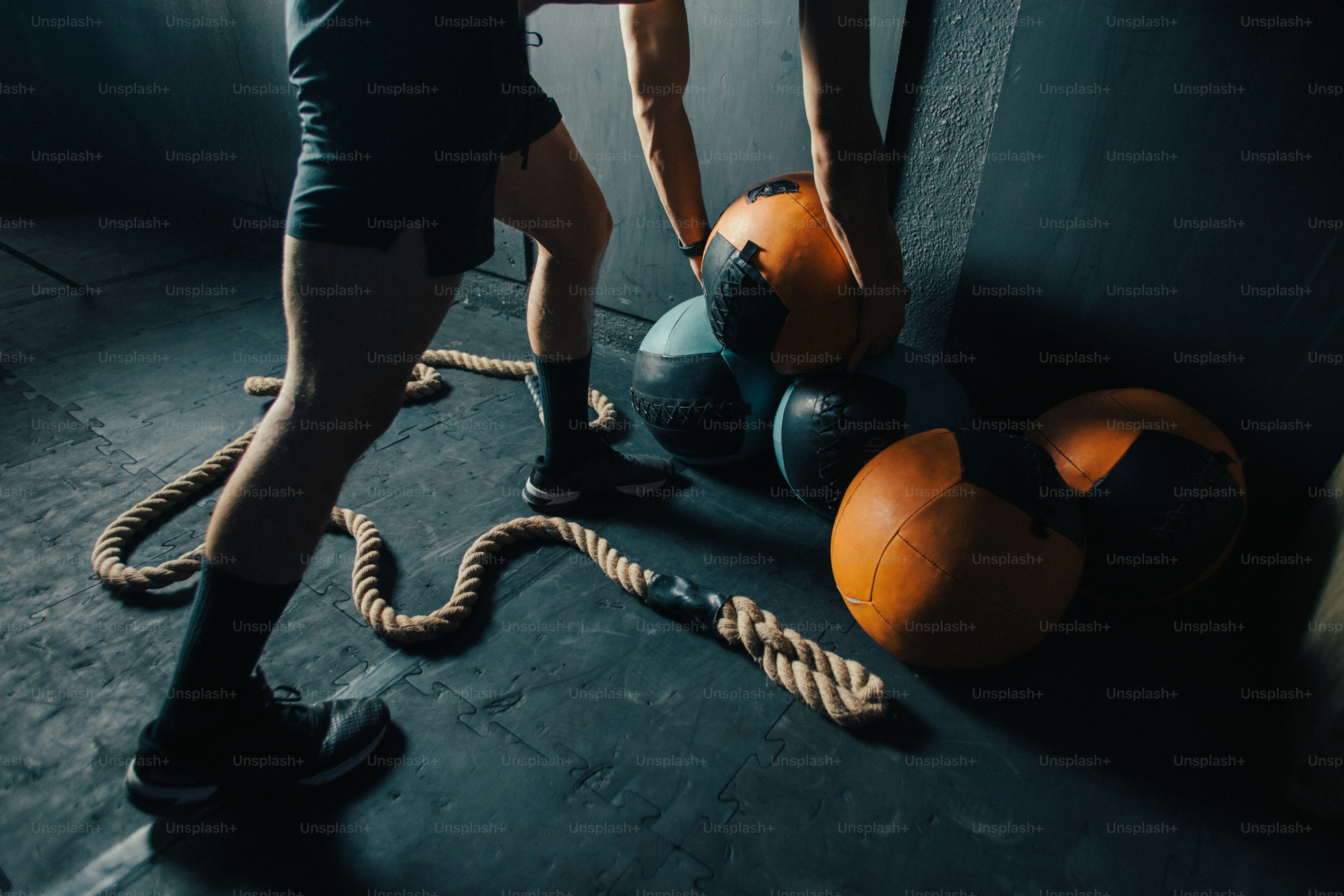 A person lifting a medicine ball near a rope on a gym floor