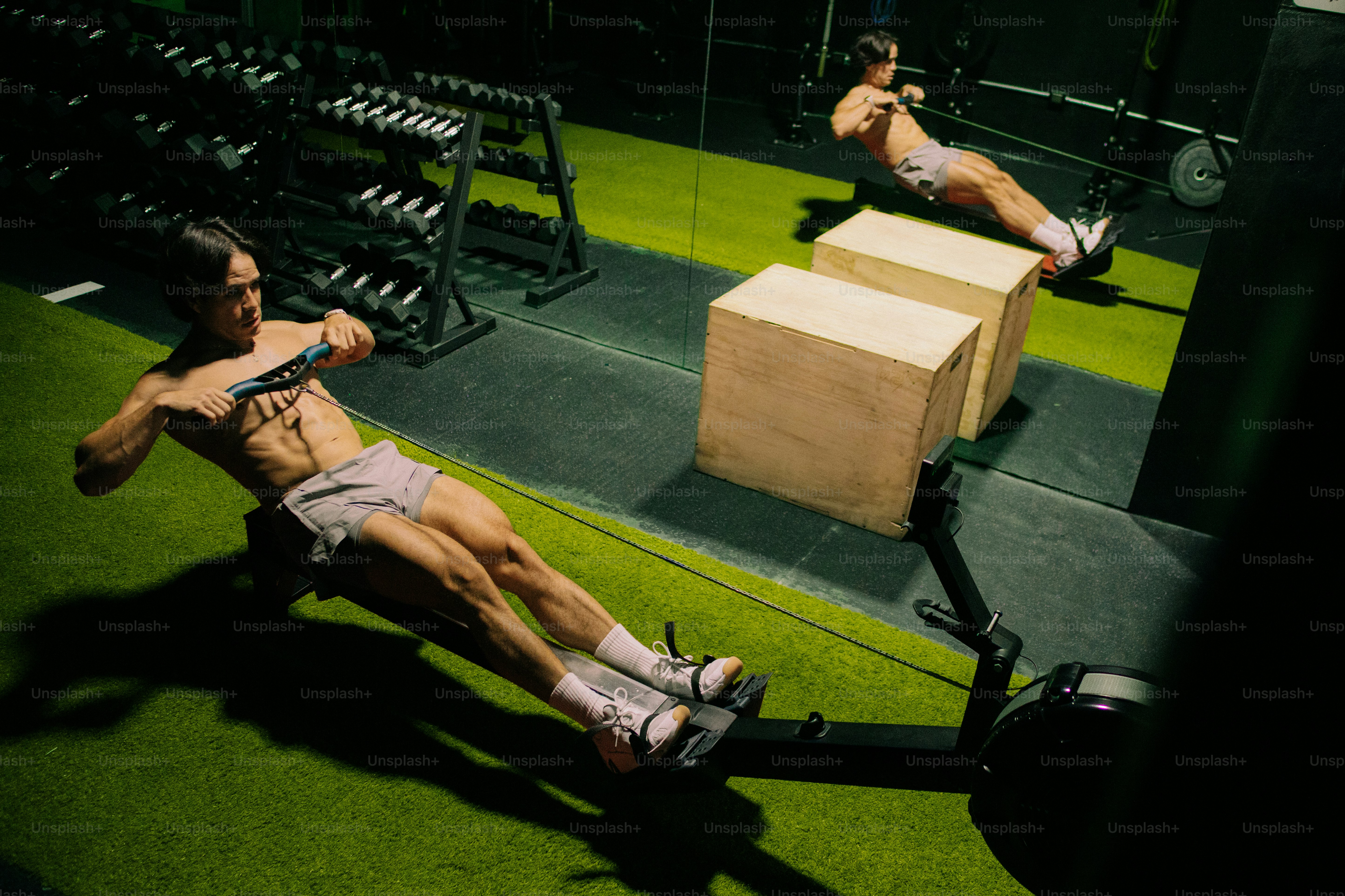 A man using a rowing machine on green turf in a gym