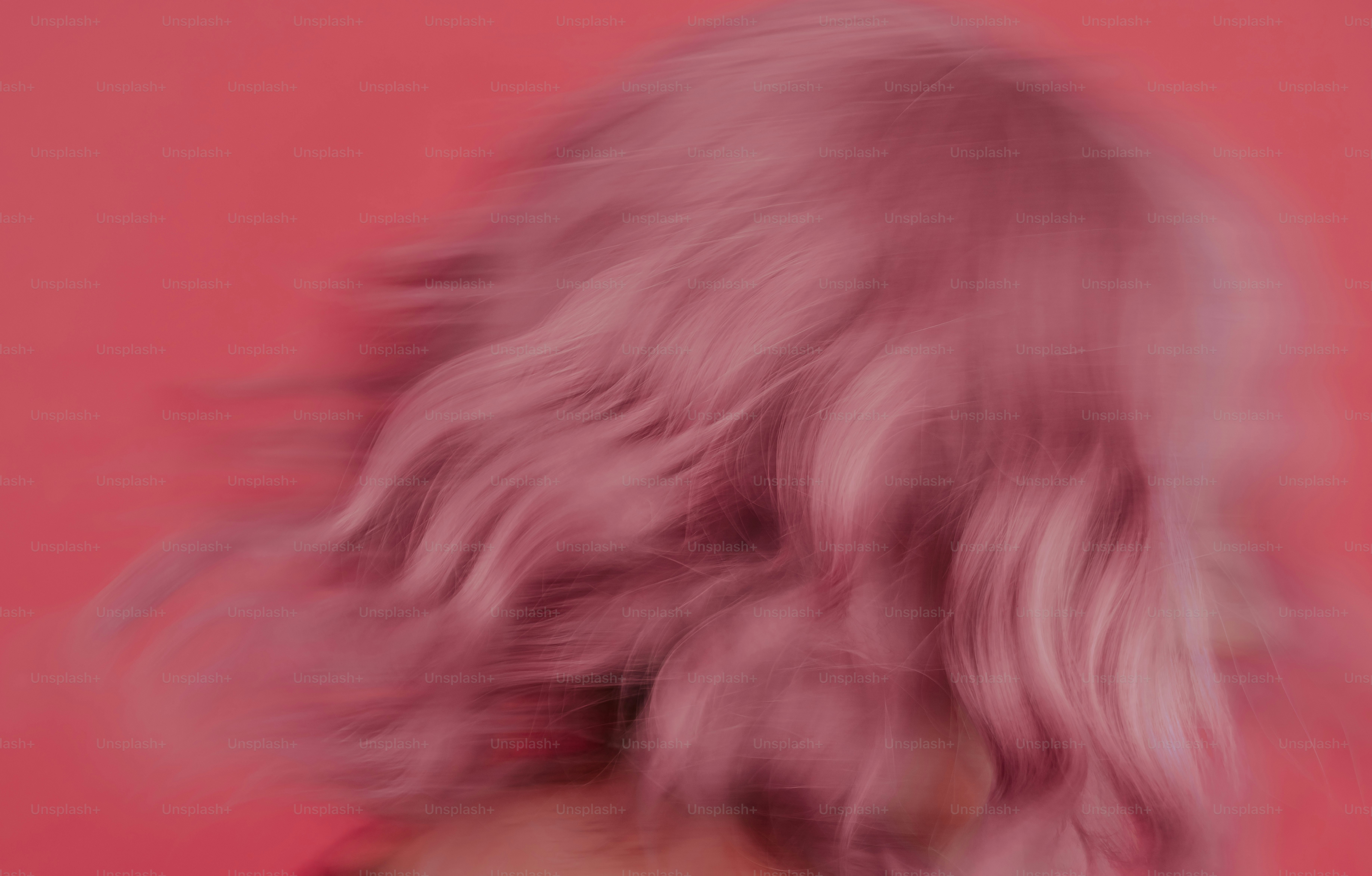 A person with wavy pink hair in motion against a solid pink background