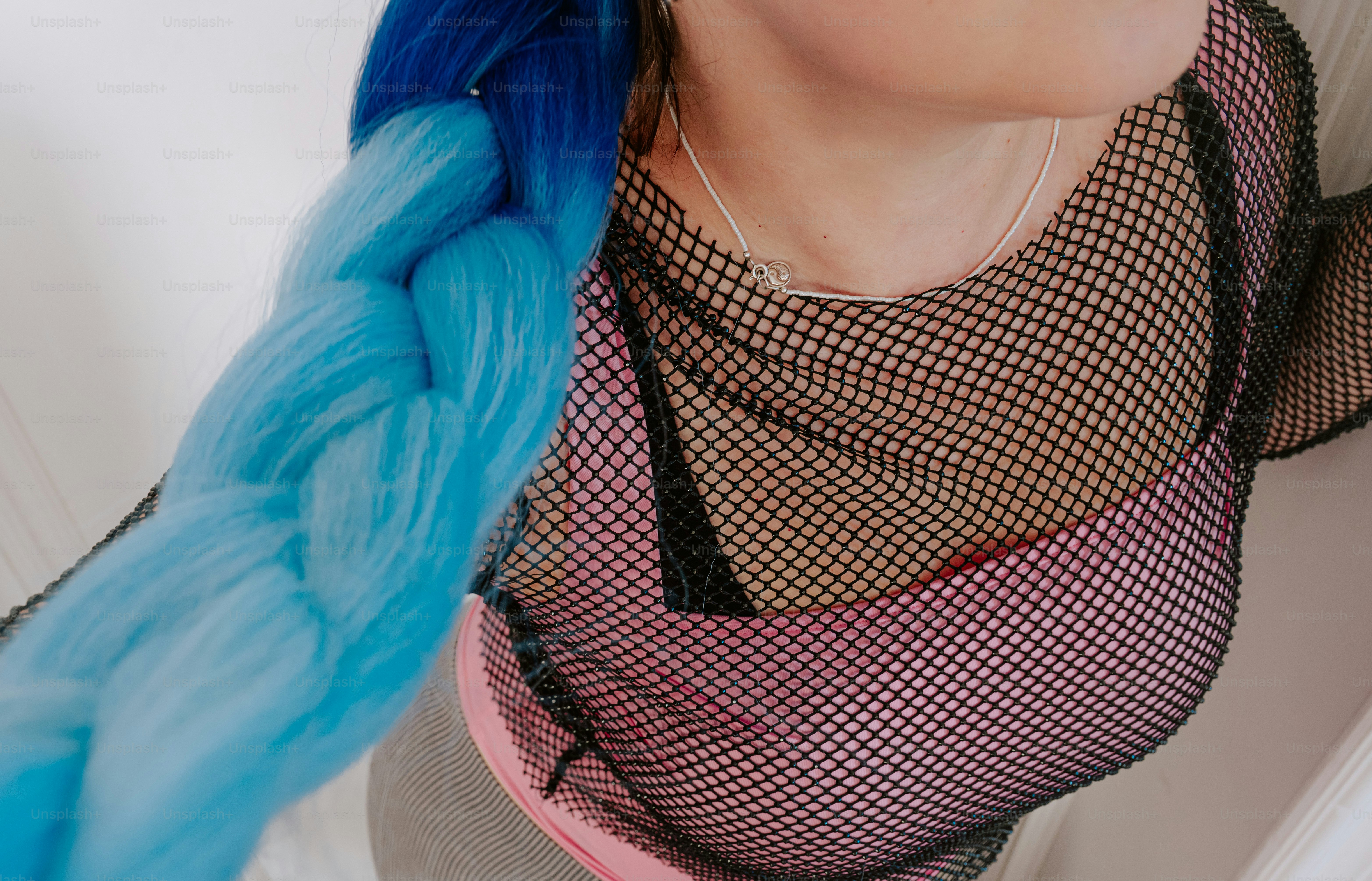 A person with a thick blue braid wearing a black fishnet top over pink