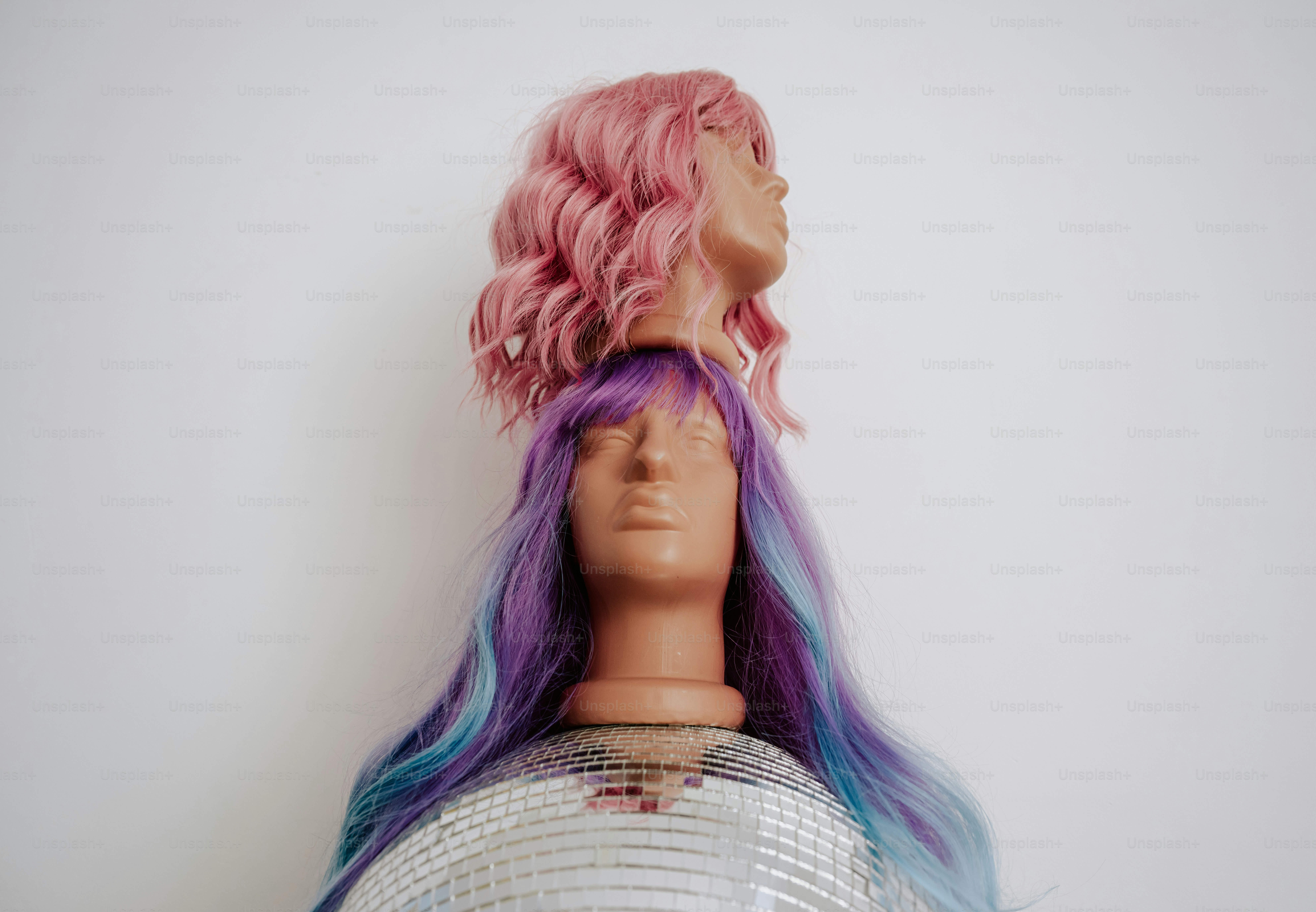 A pink wig on a mannequin head stacked atop a purple wigged mannequin