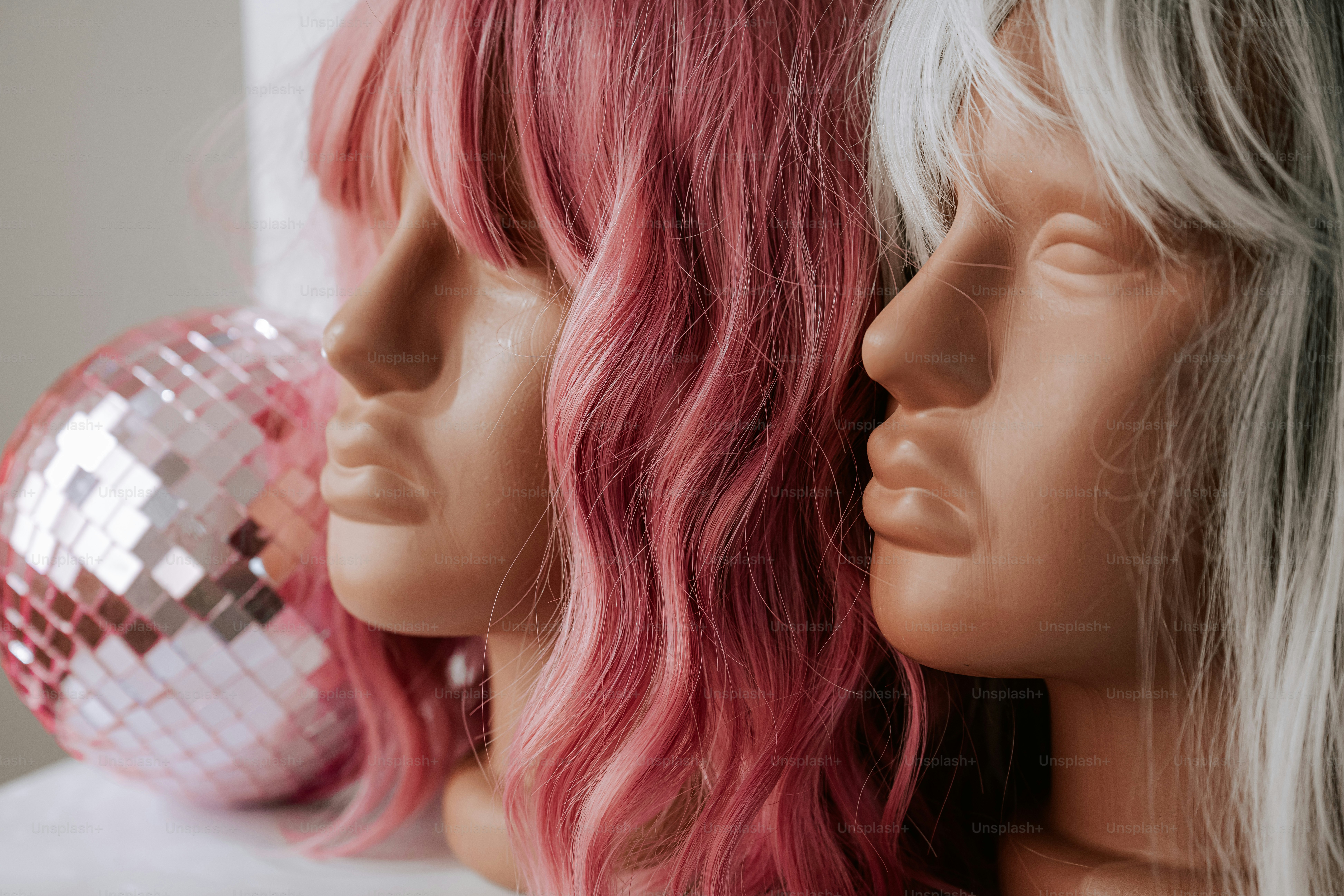 Two mannequin heads with pink and white wigs beside a pink disco ball