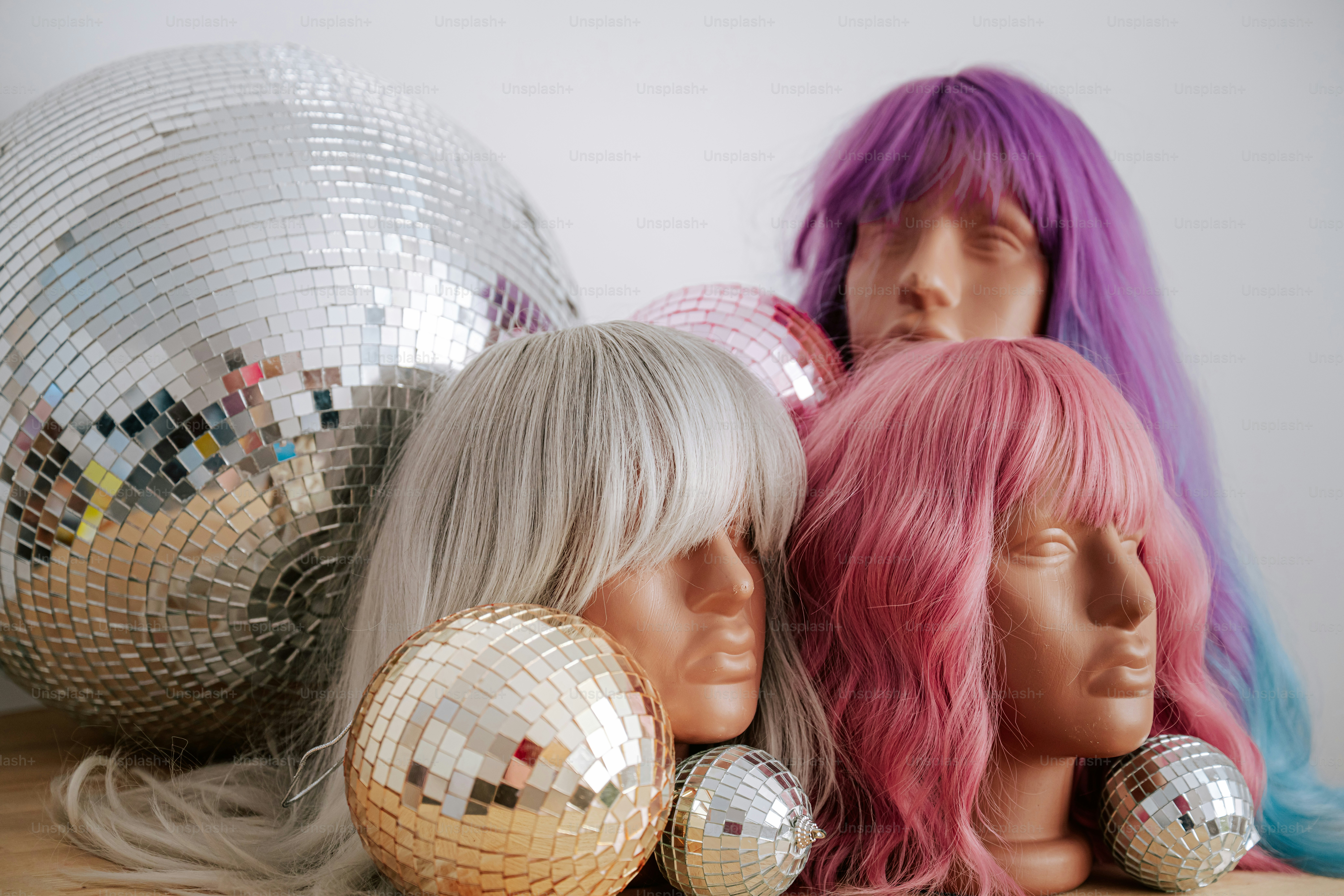 Three mannequin heads with colorful wigs beside several reflective disco balls