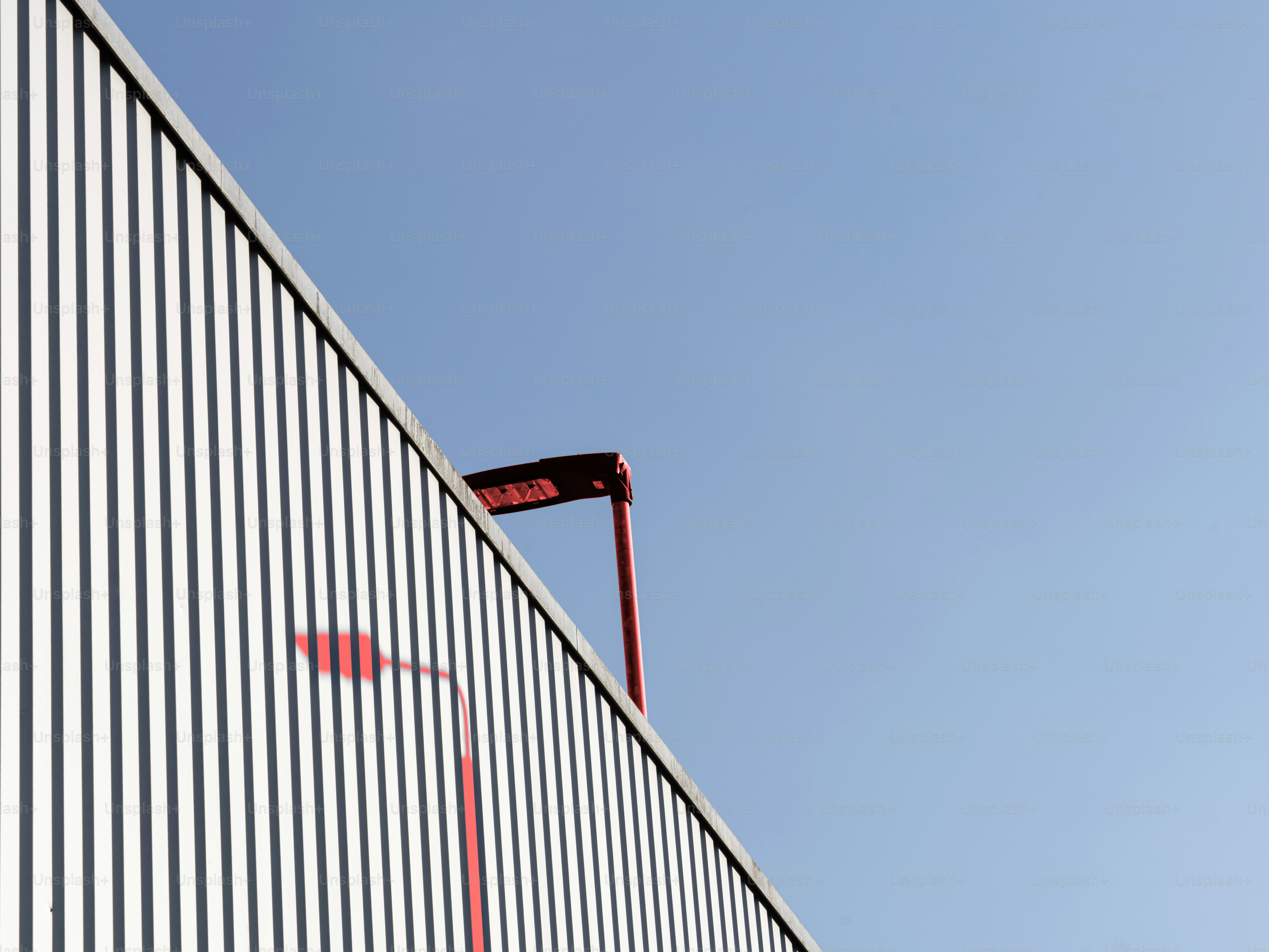 A red street lamp casting a shadow on a white corrugated metal wall