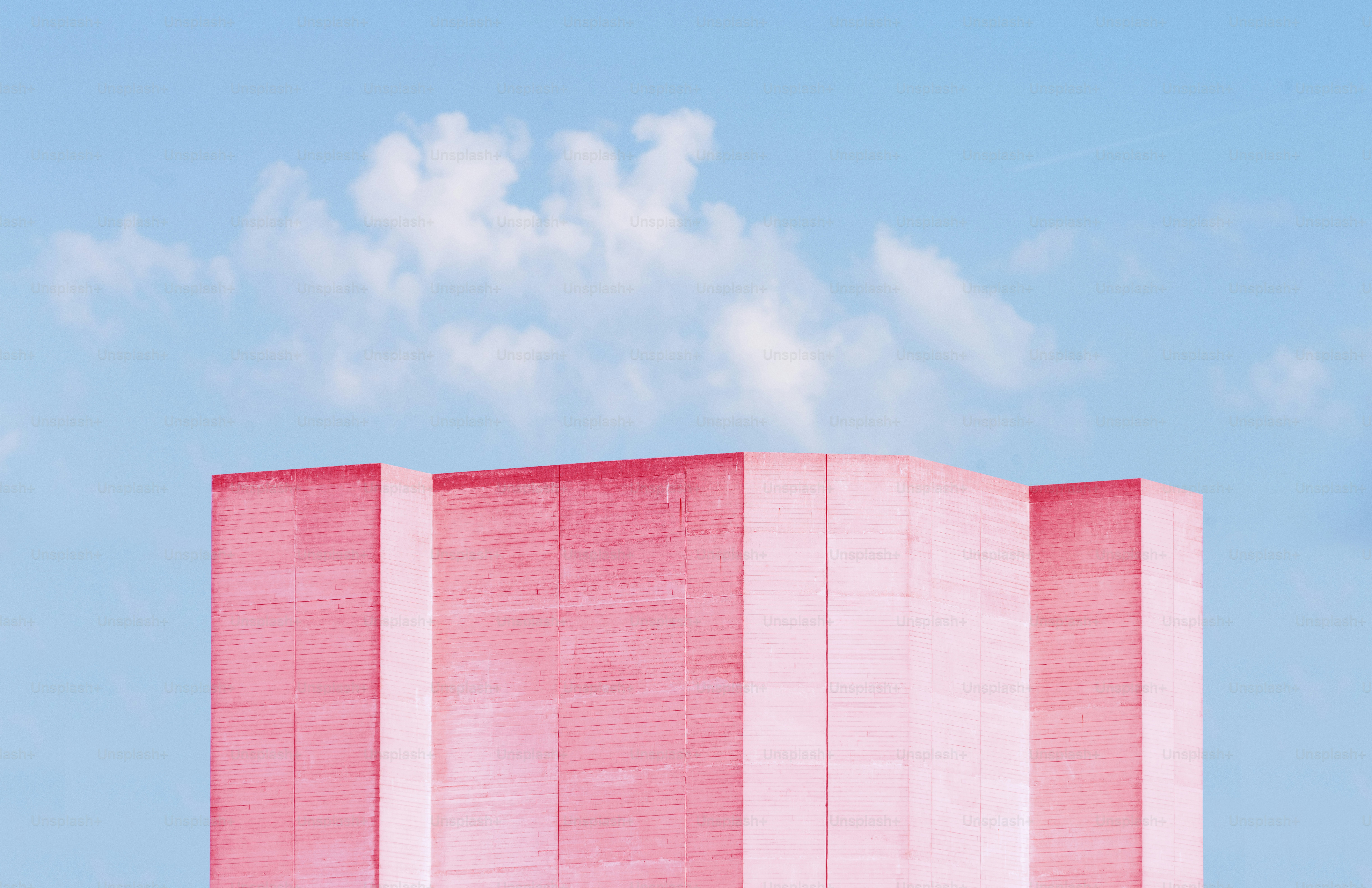 A pink concrete building facade against a bright blue sky with white clouds