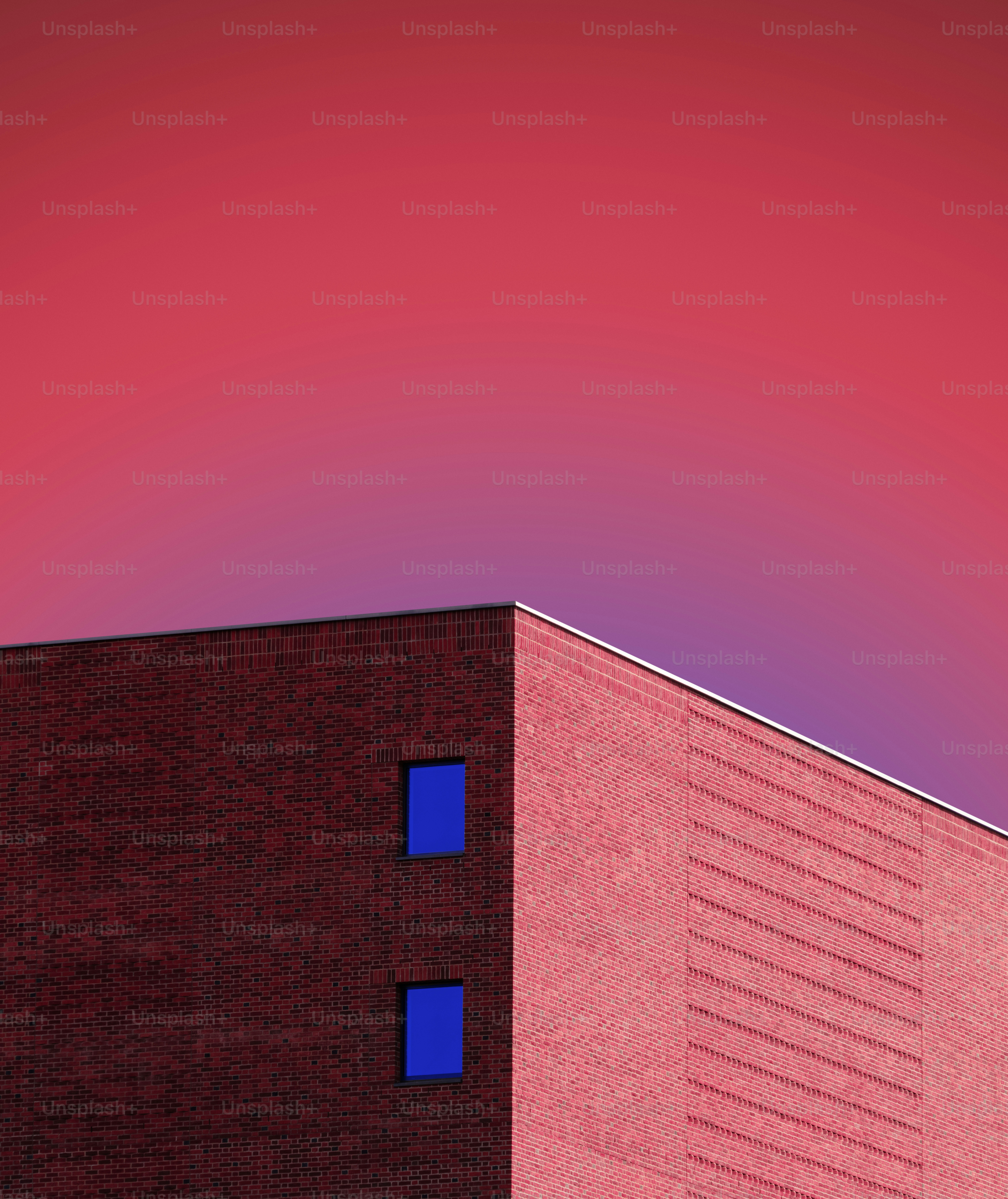 A red brick building corner with two blue windows against a pink sky