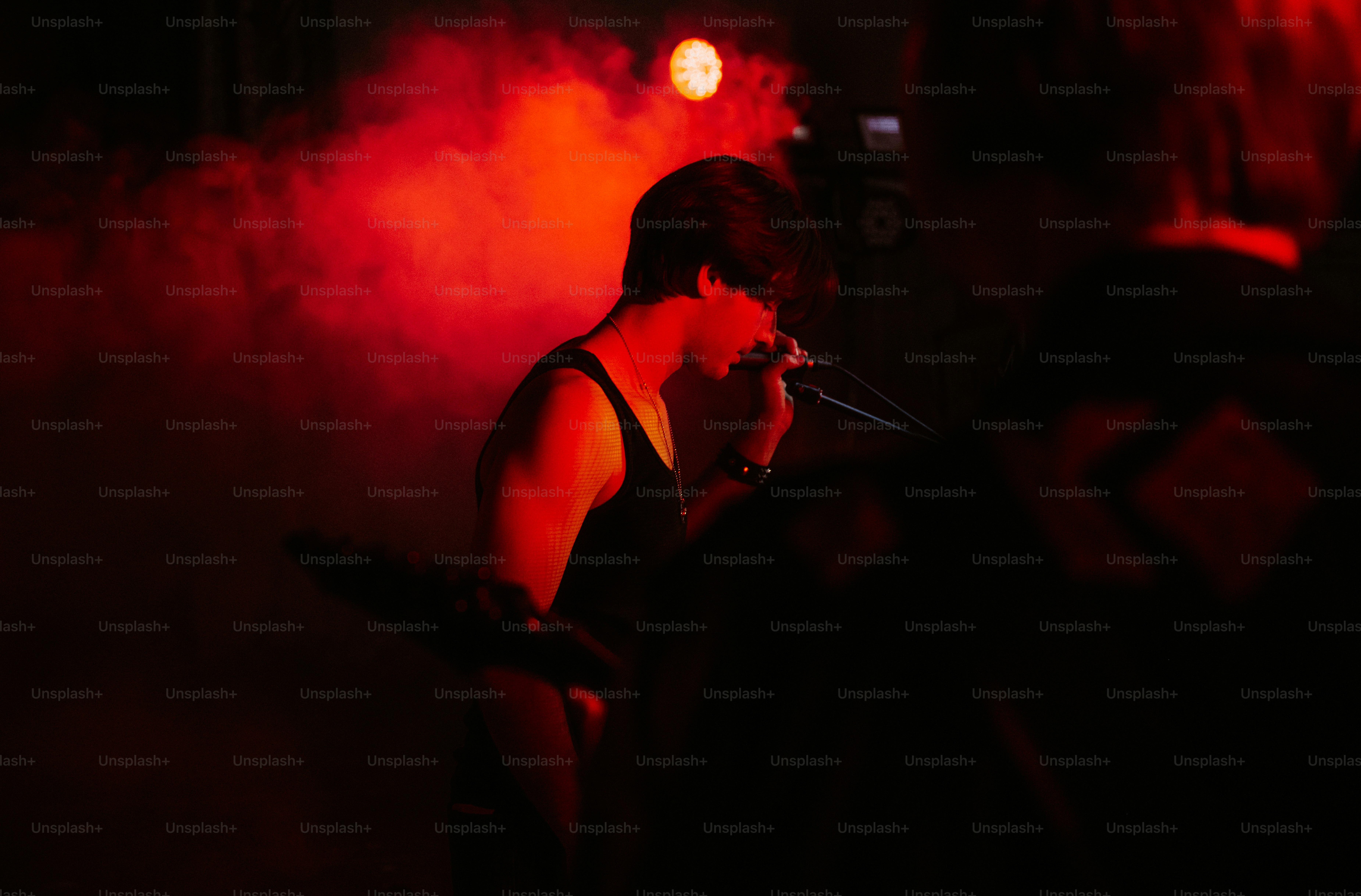 A person singing into a microphone on a stage filled with red smoke