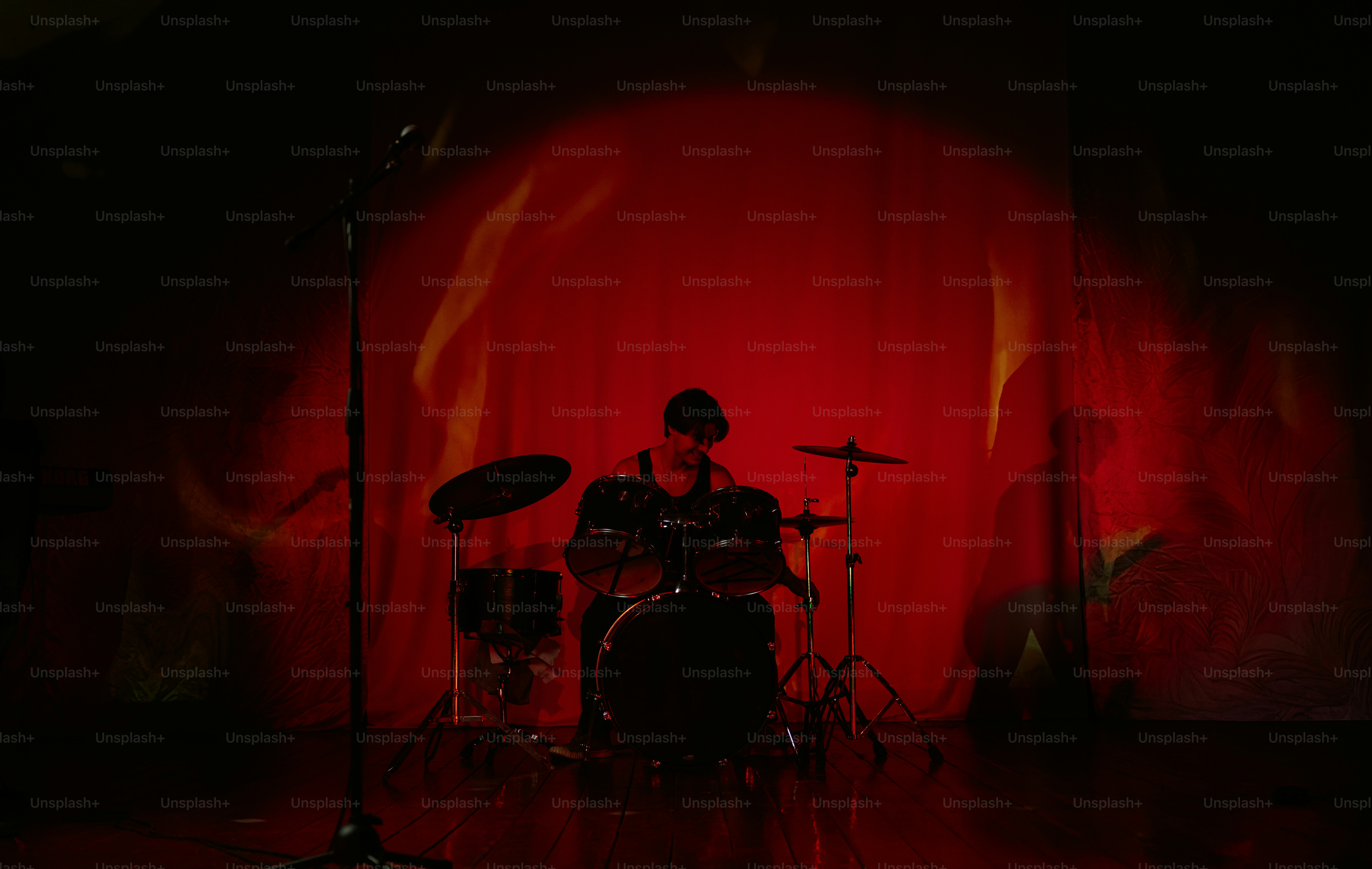 A drummer playing a drum kit on a stage with red lighting