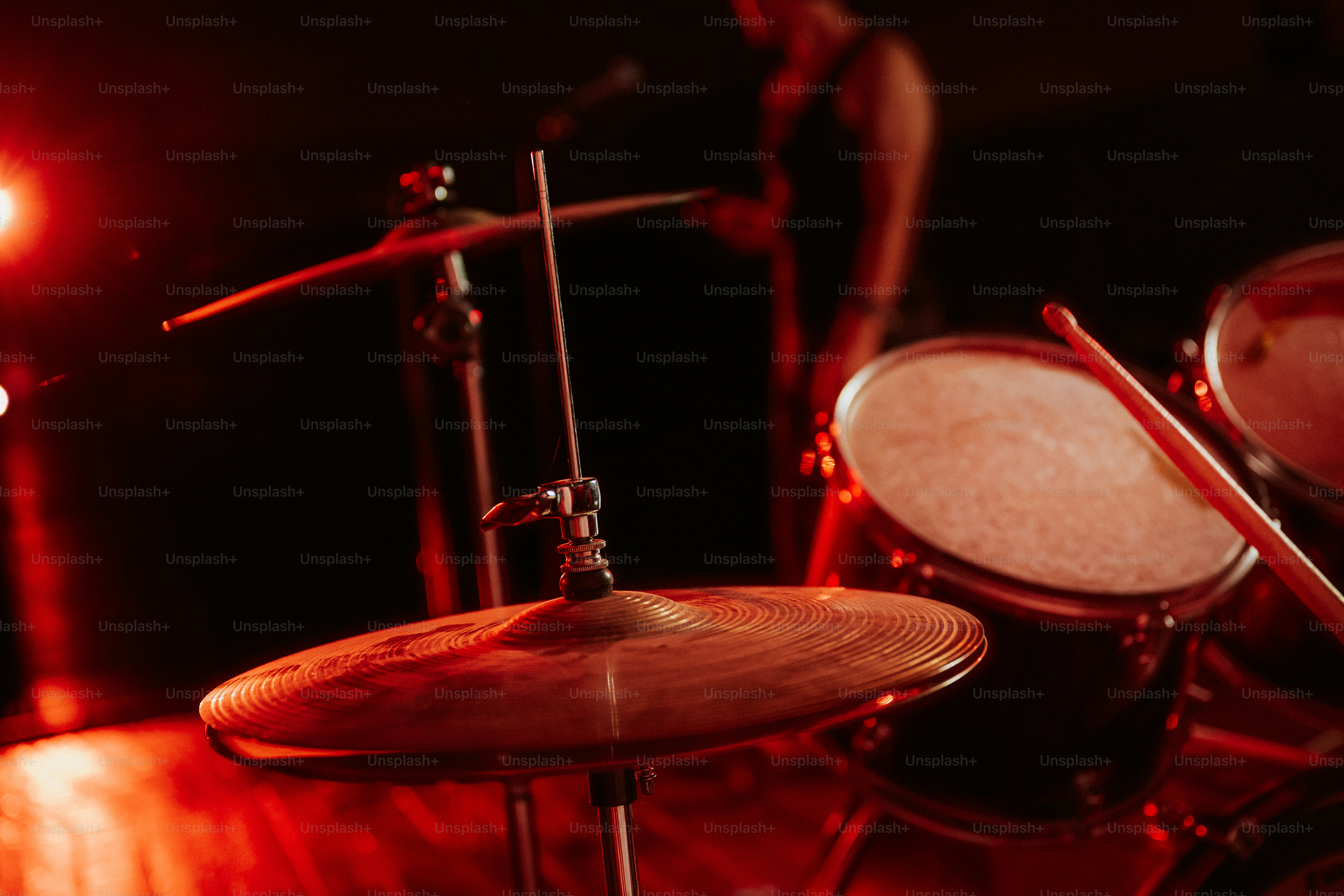 A drum cymbal and snare drum on a stage under red lighting