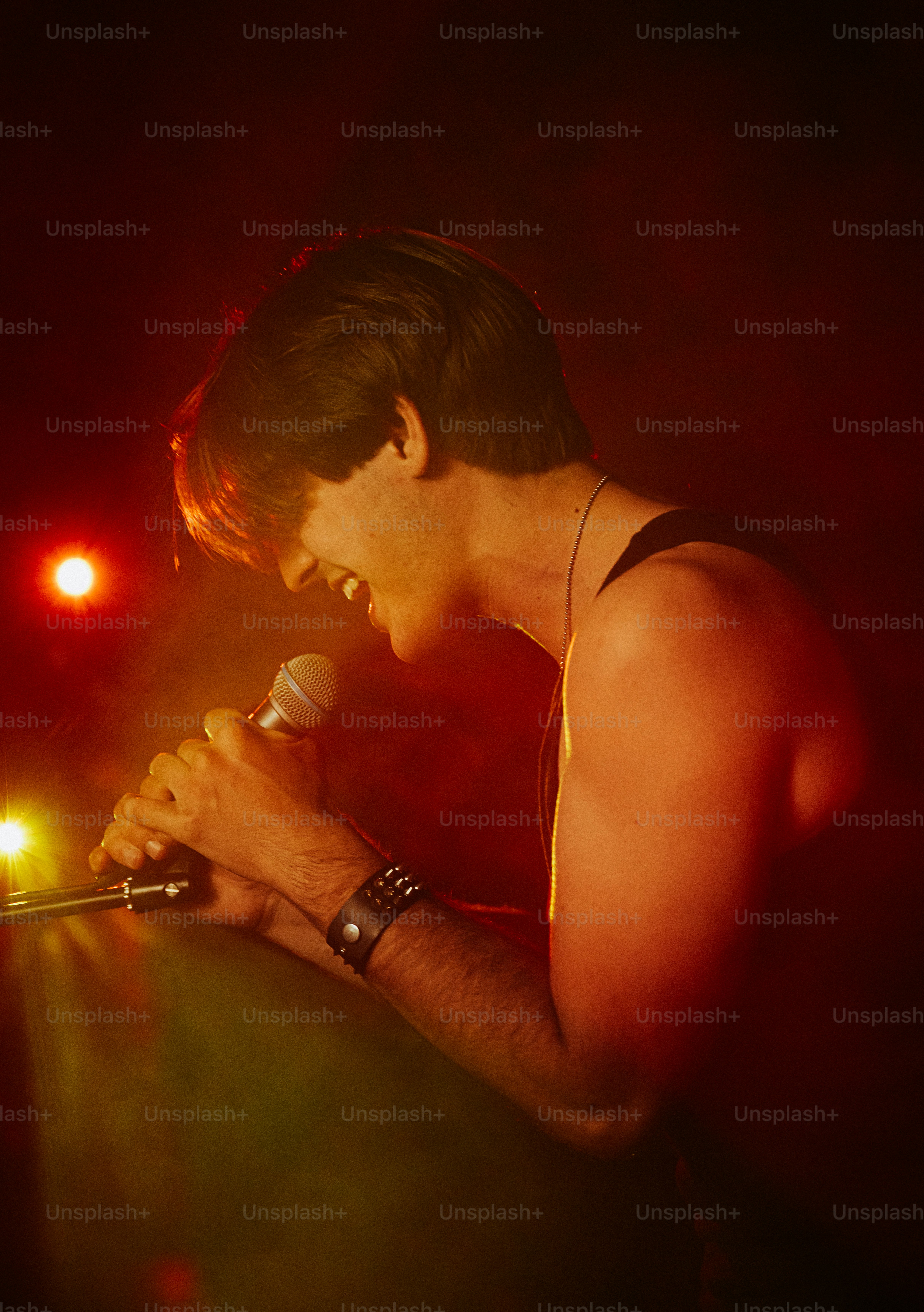 A person singing into a microphone on a stage with warm red lighting
