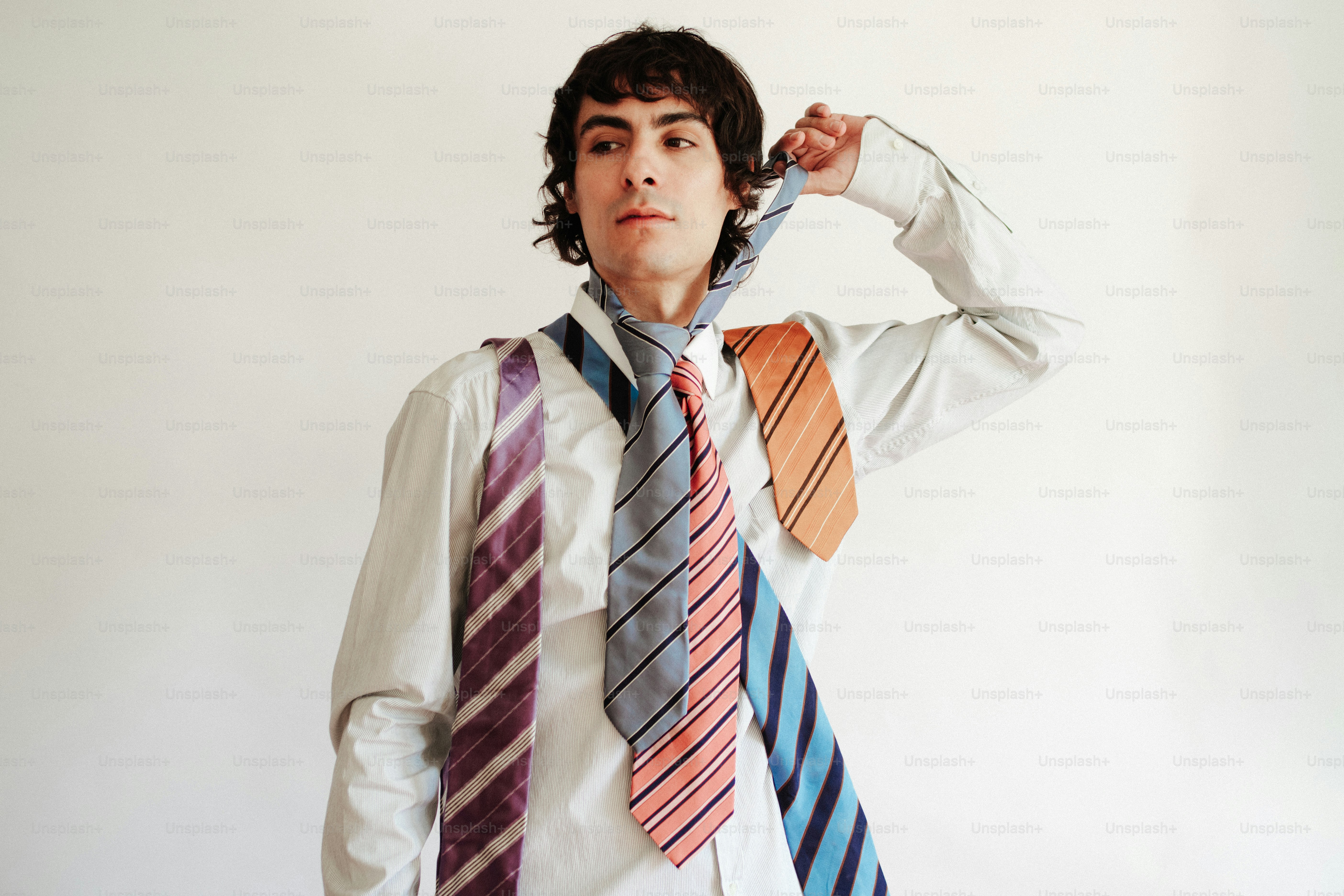 Um homem de camisa branca usando várias gravatas listradas coloridas ao redor do pescoço
