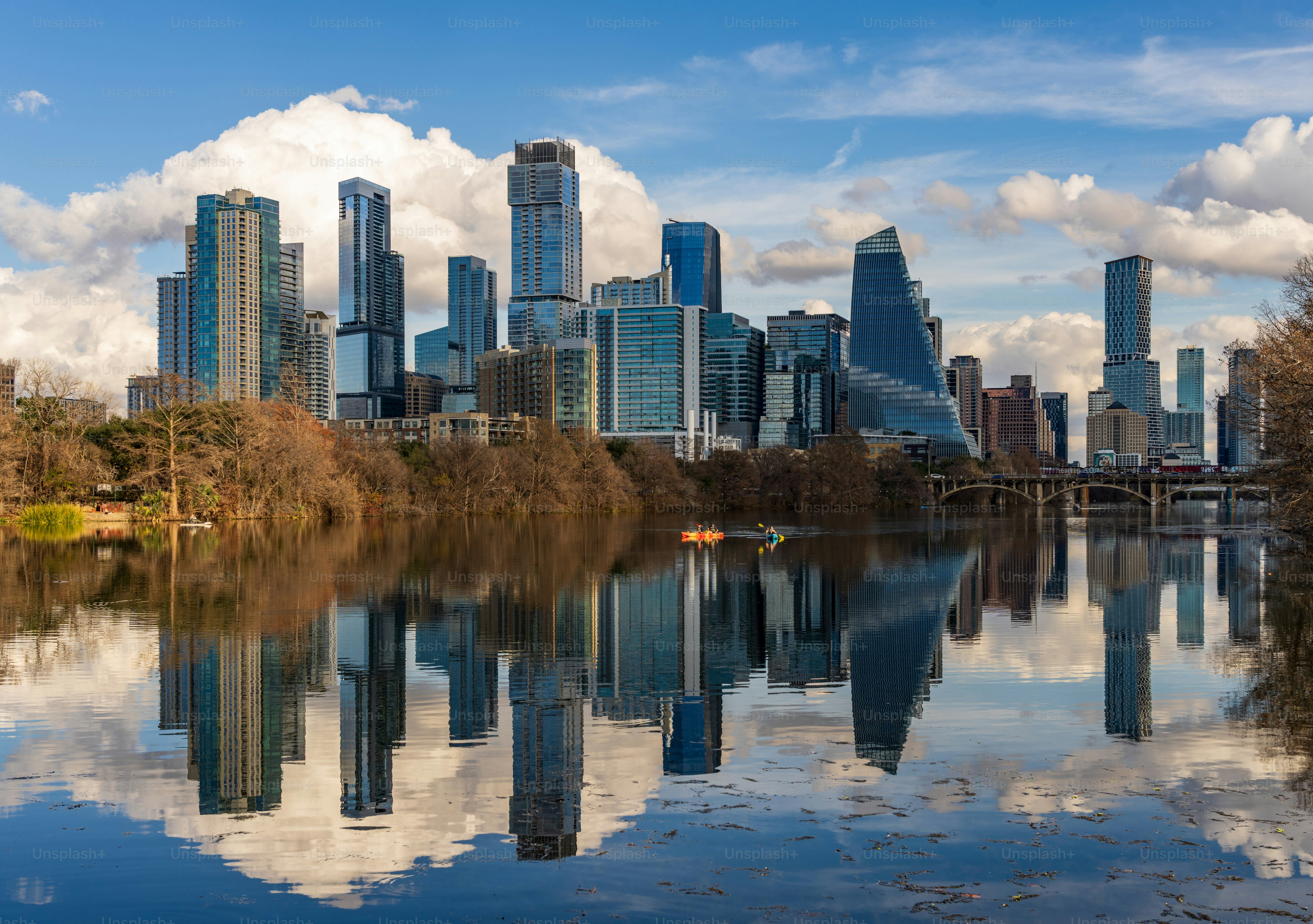 Clouds hover over the Austin skyline as buildings reflect on the calm waters of the Colorado river during late afternoon.