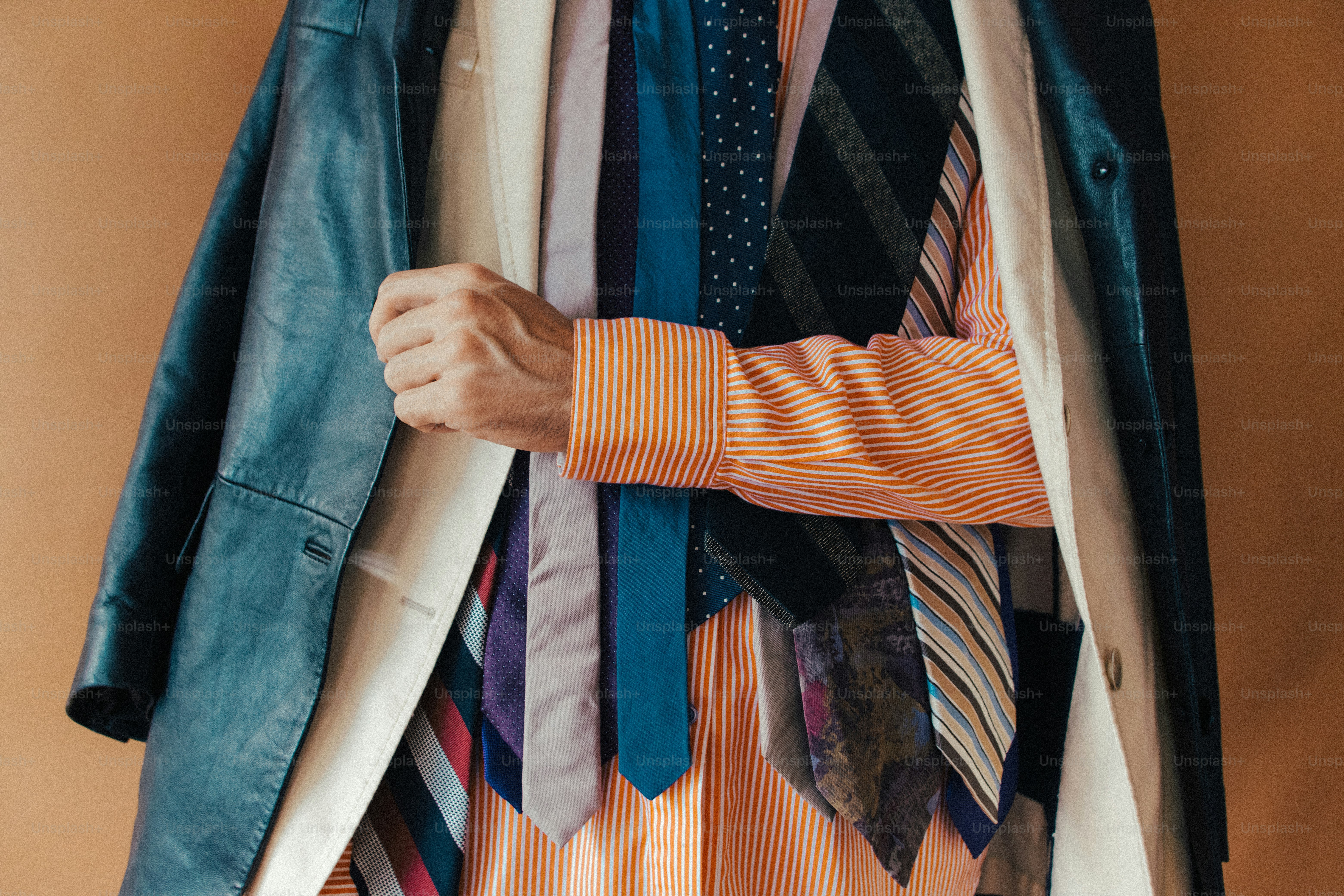 Una persona che indossa una camicia a righe arancioni e più cravatte sotto una giacca di pelle