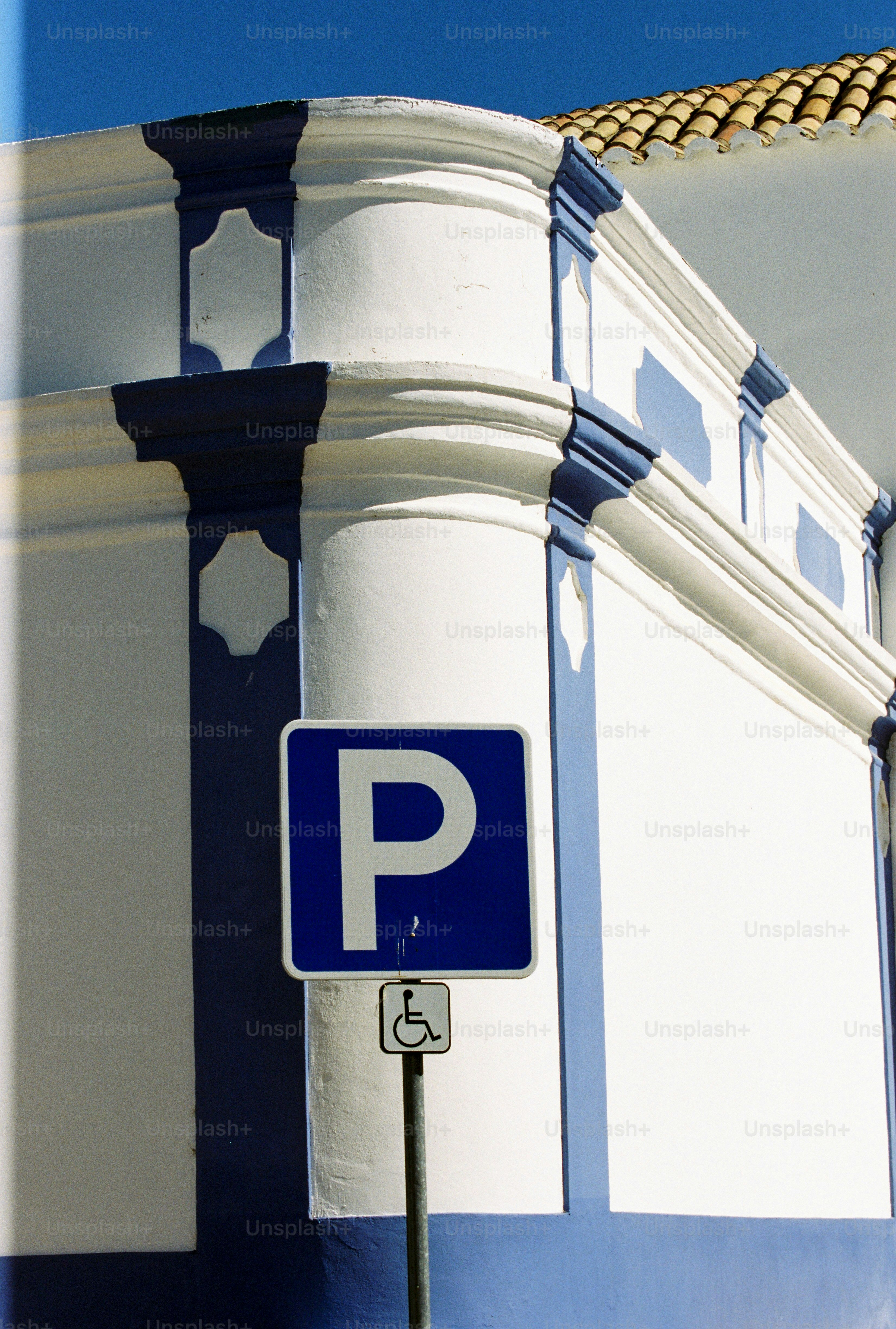 Un cartel de aparcamiento azul con un símbolo de silla de ruedas contra un edificio blanco en Alvor