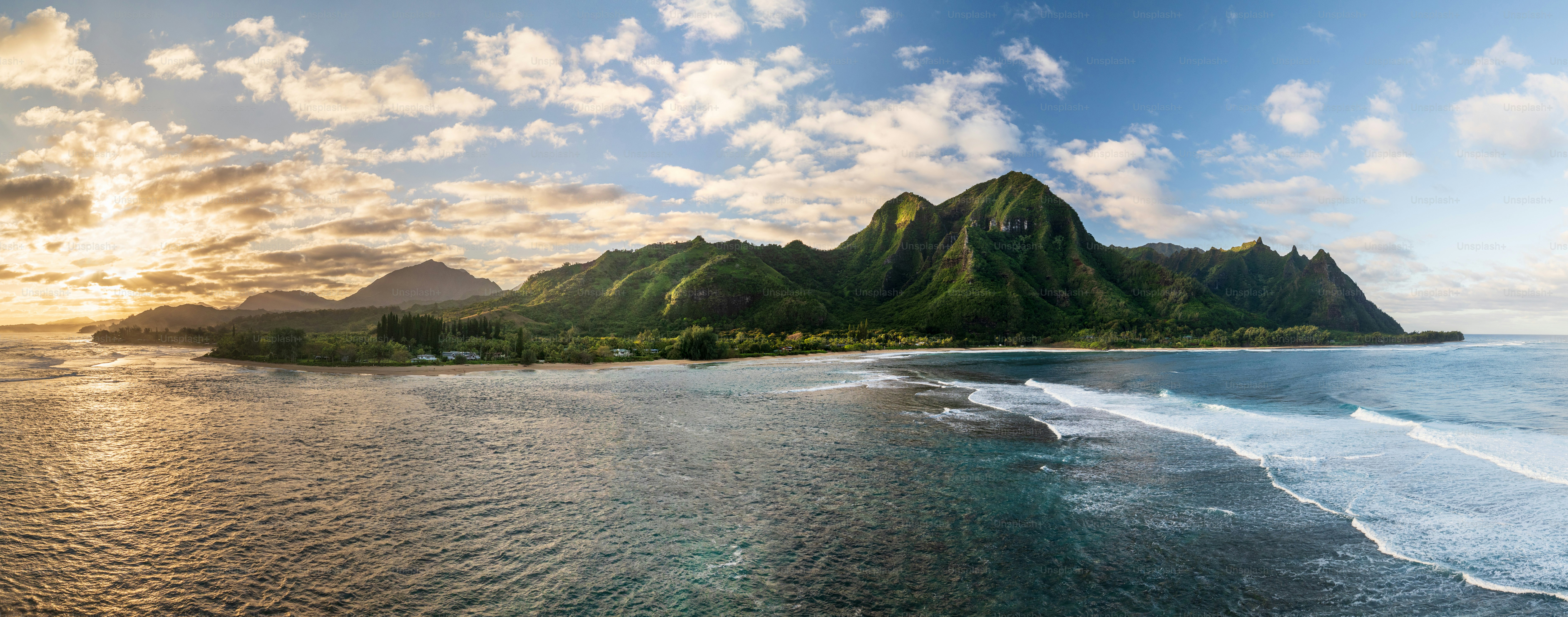 Tunnels Beach panorama view from above at sunset, with the clear turquoise water and lush green mountains in the background