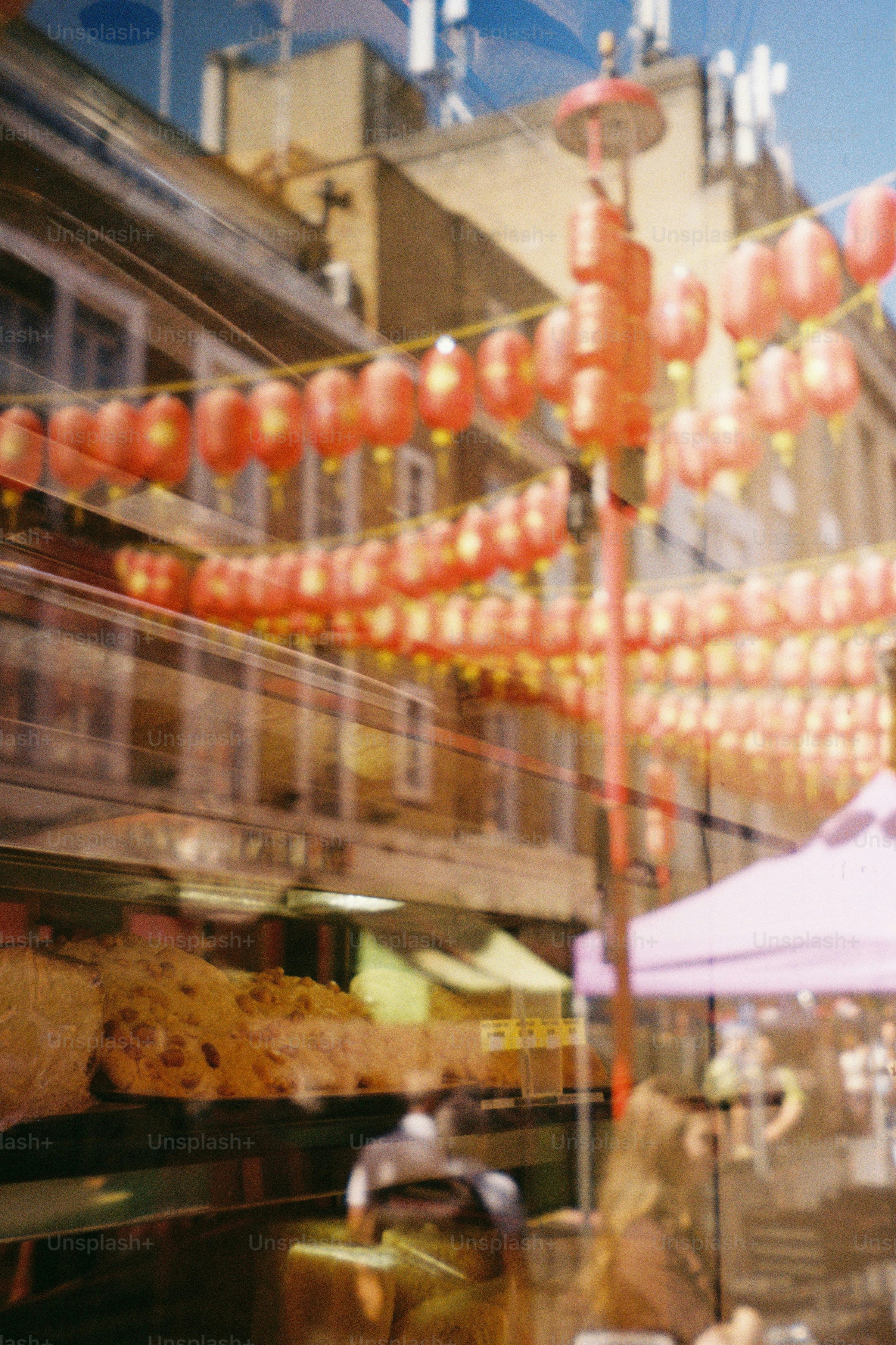 Red lanterns and buildings reflected in a shop window with baked goods