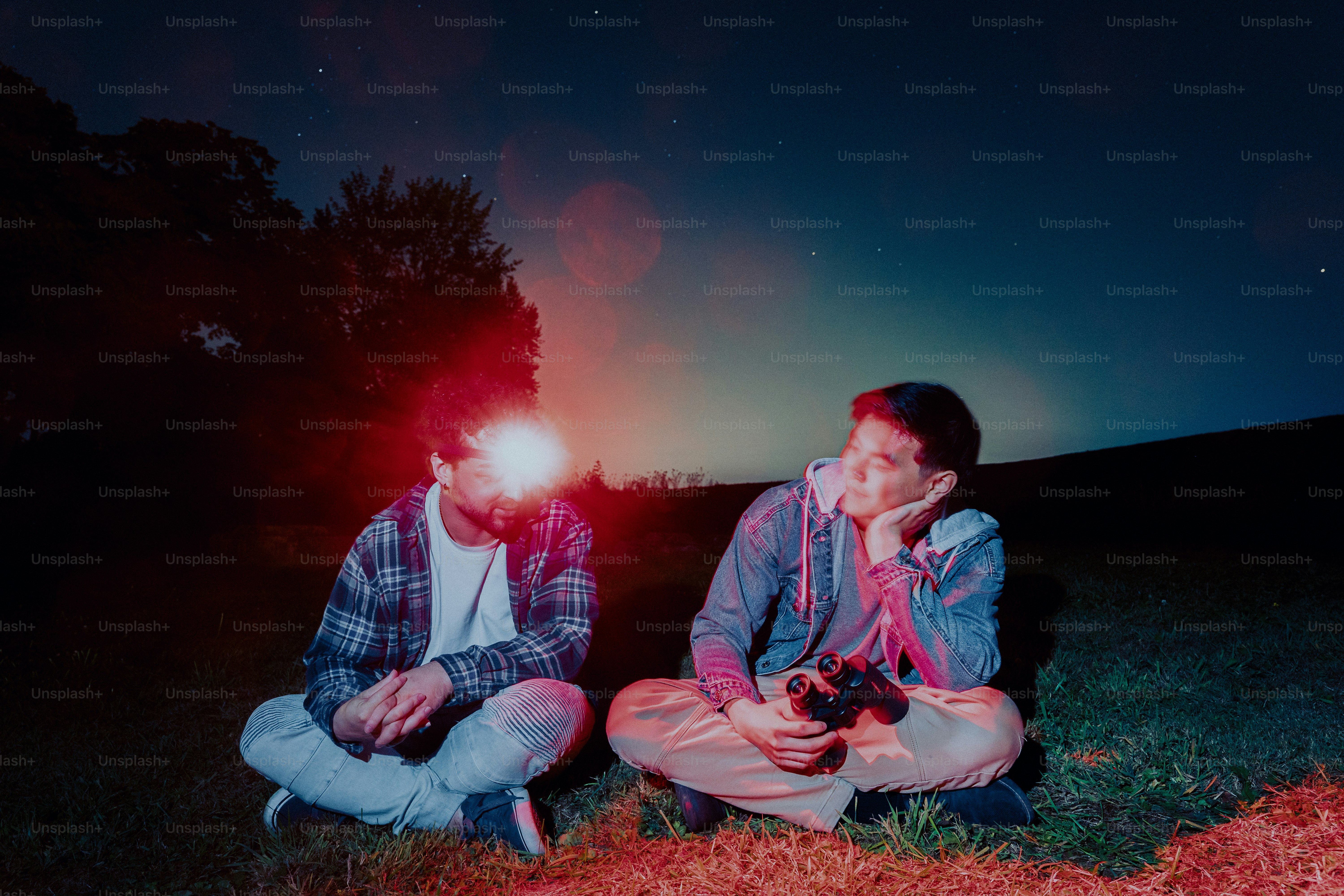 Due persone sedute sull'erba di notte con una lampada frontale brillante e un binocolo