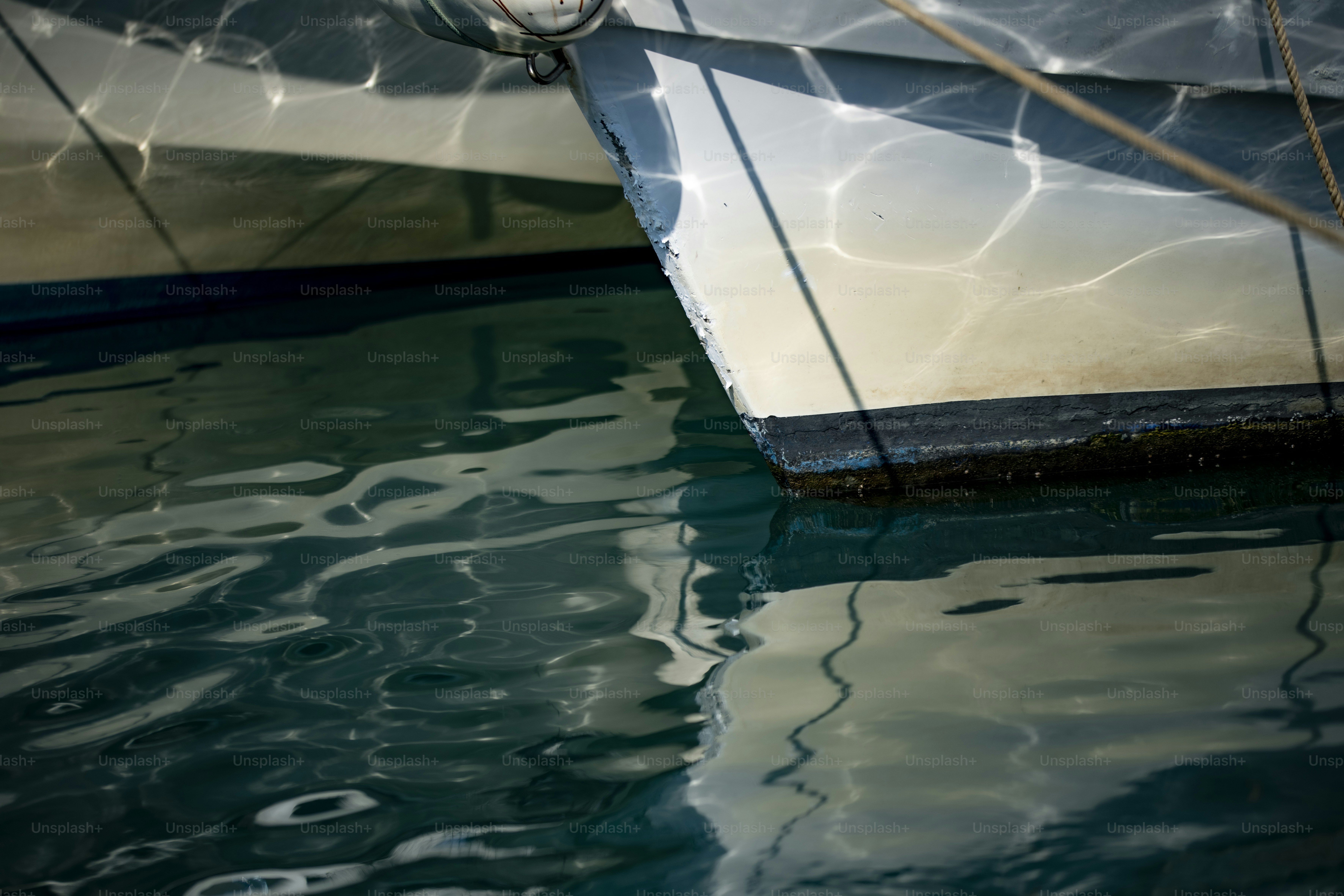 The white hull of a boat reflecting sunlight on dark rippling water