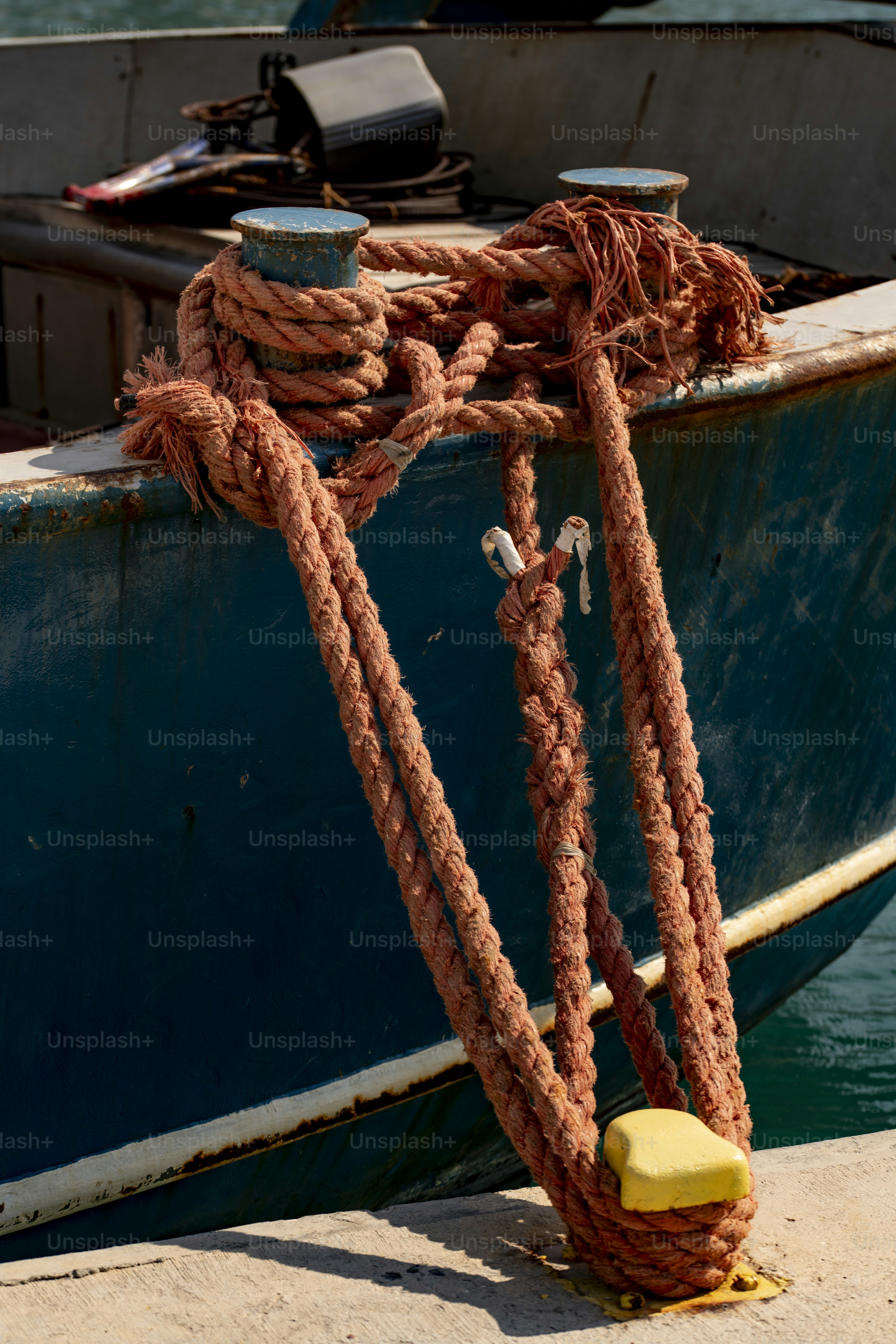 Thick orange rope coiled around a blue boat cleat and a yellow dock bollard