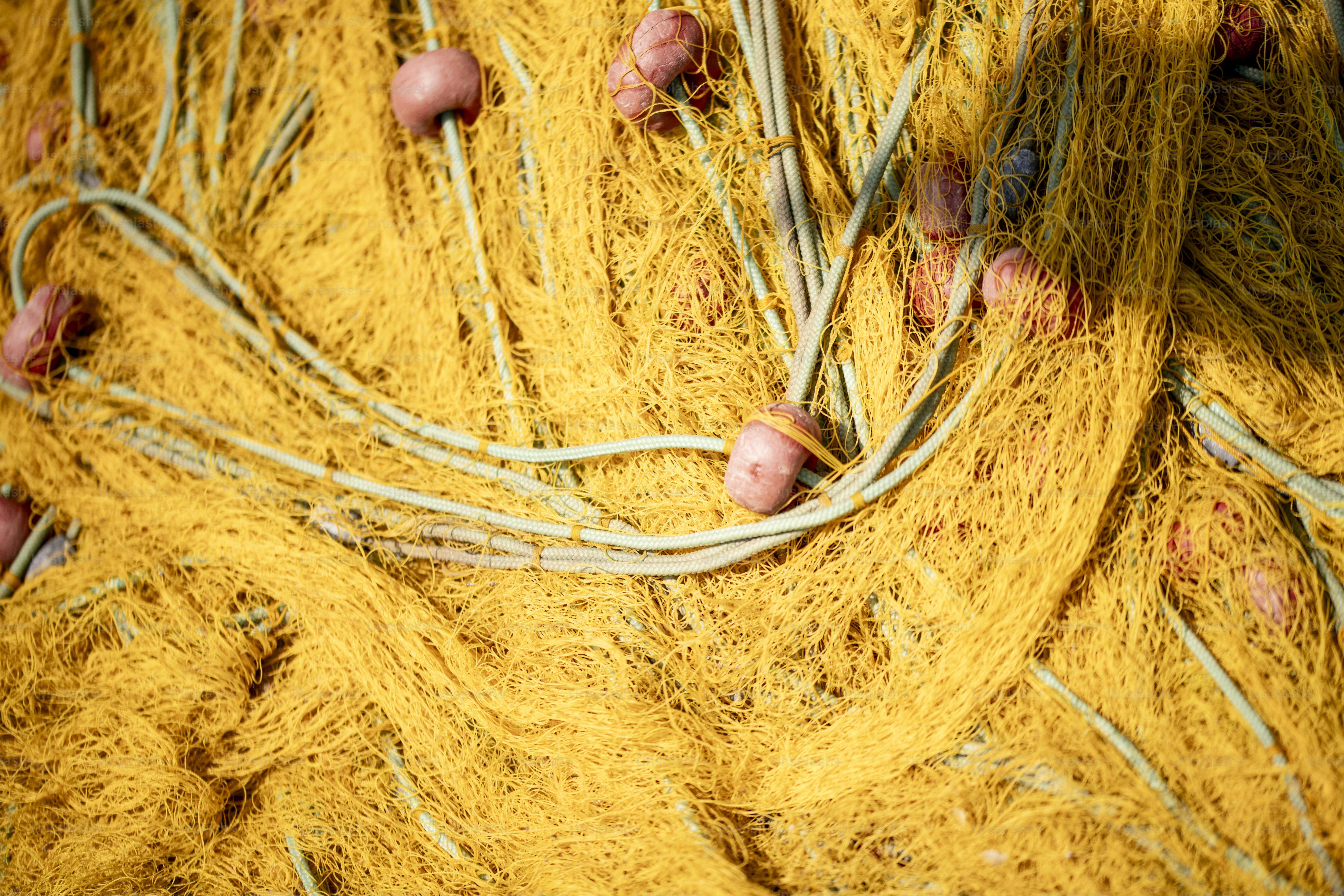 A pile of yellow fishing nets with red floats and white ropes