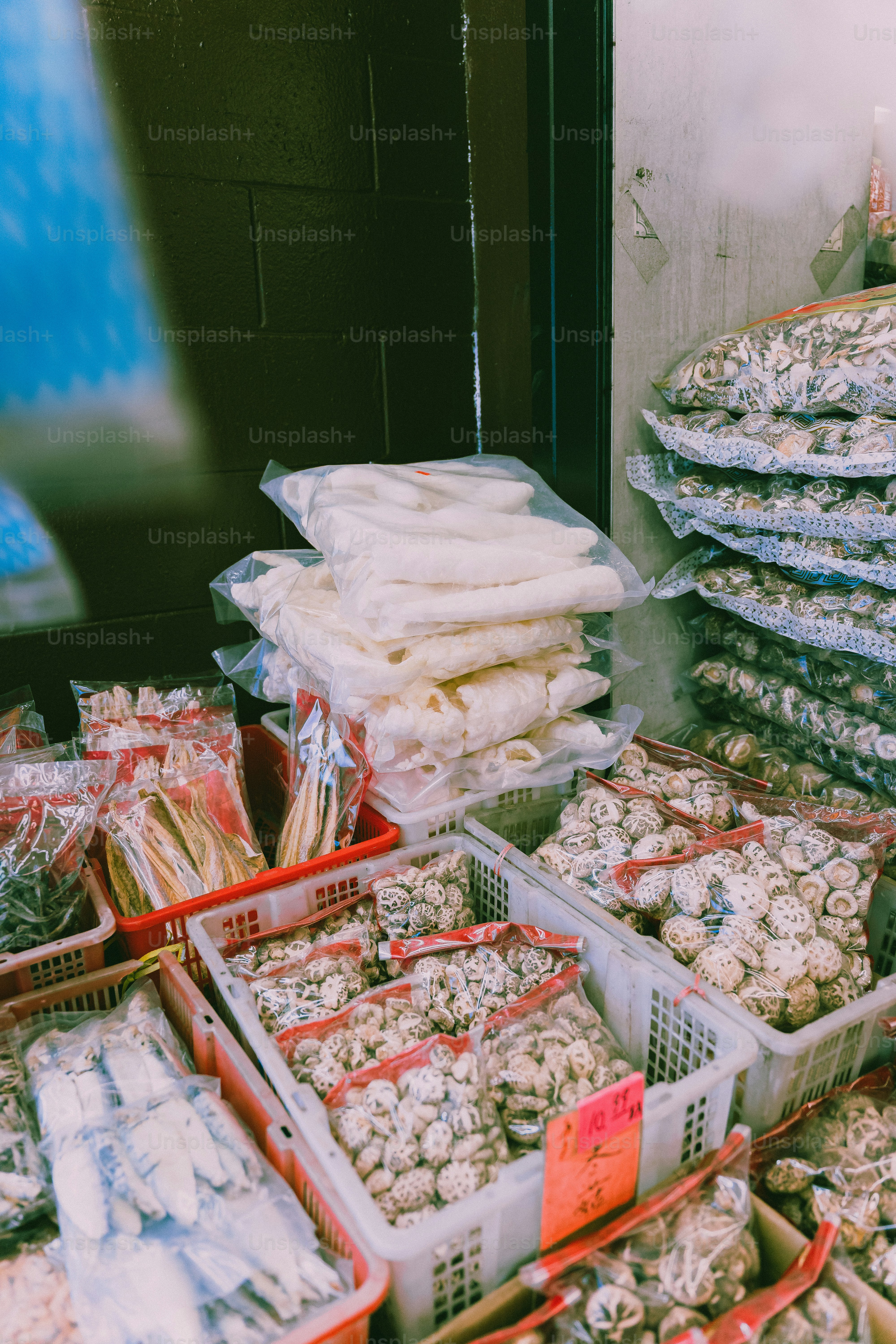 Plastic bags of dried mushrooms and white seafood in crates at a market