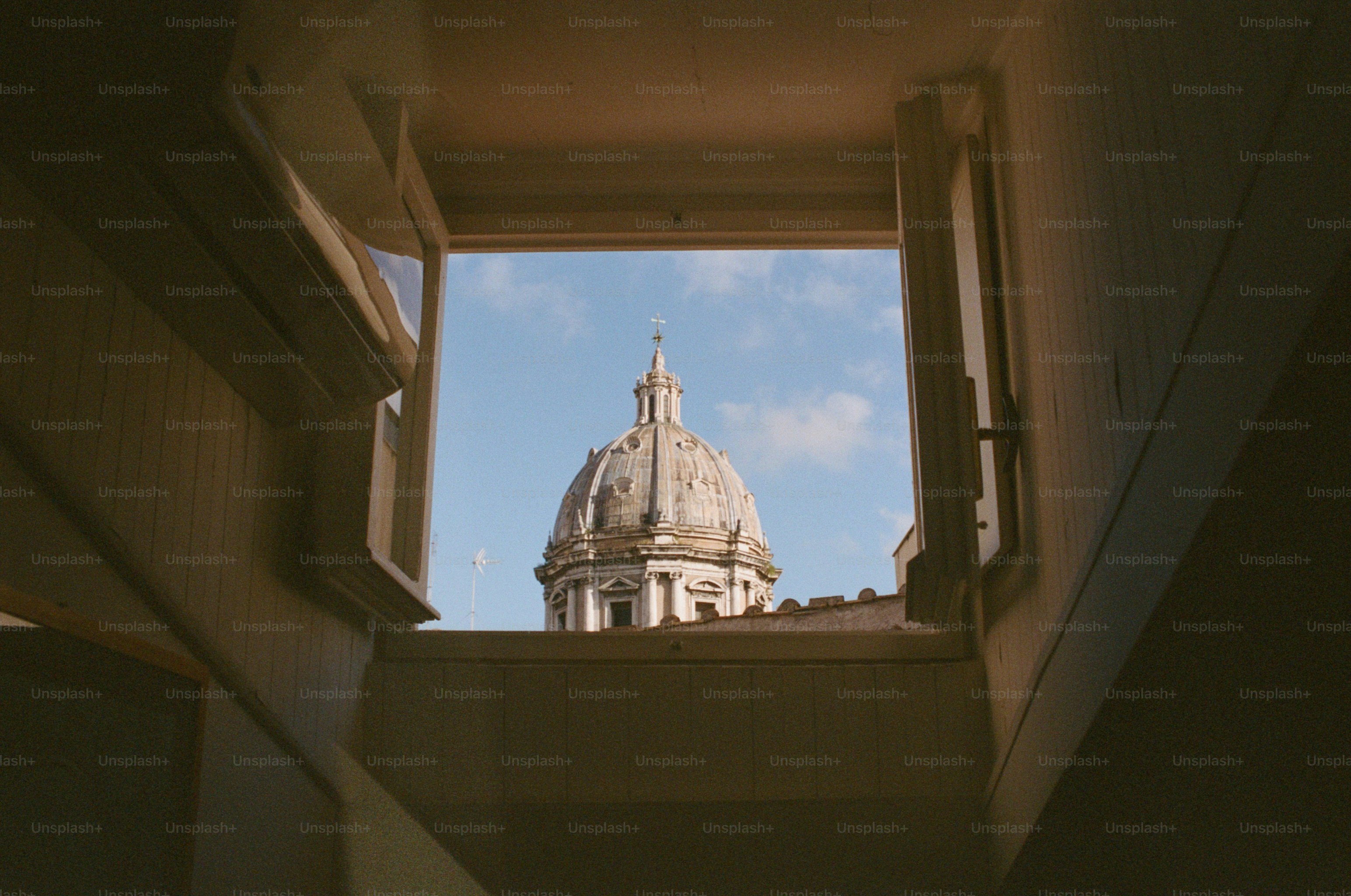 A baroque cathedral dome with a cross seen through an open wooden window