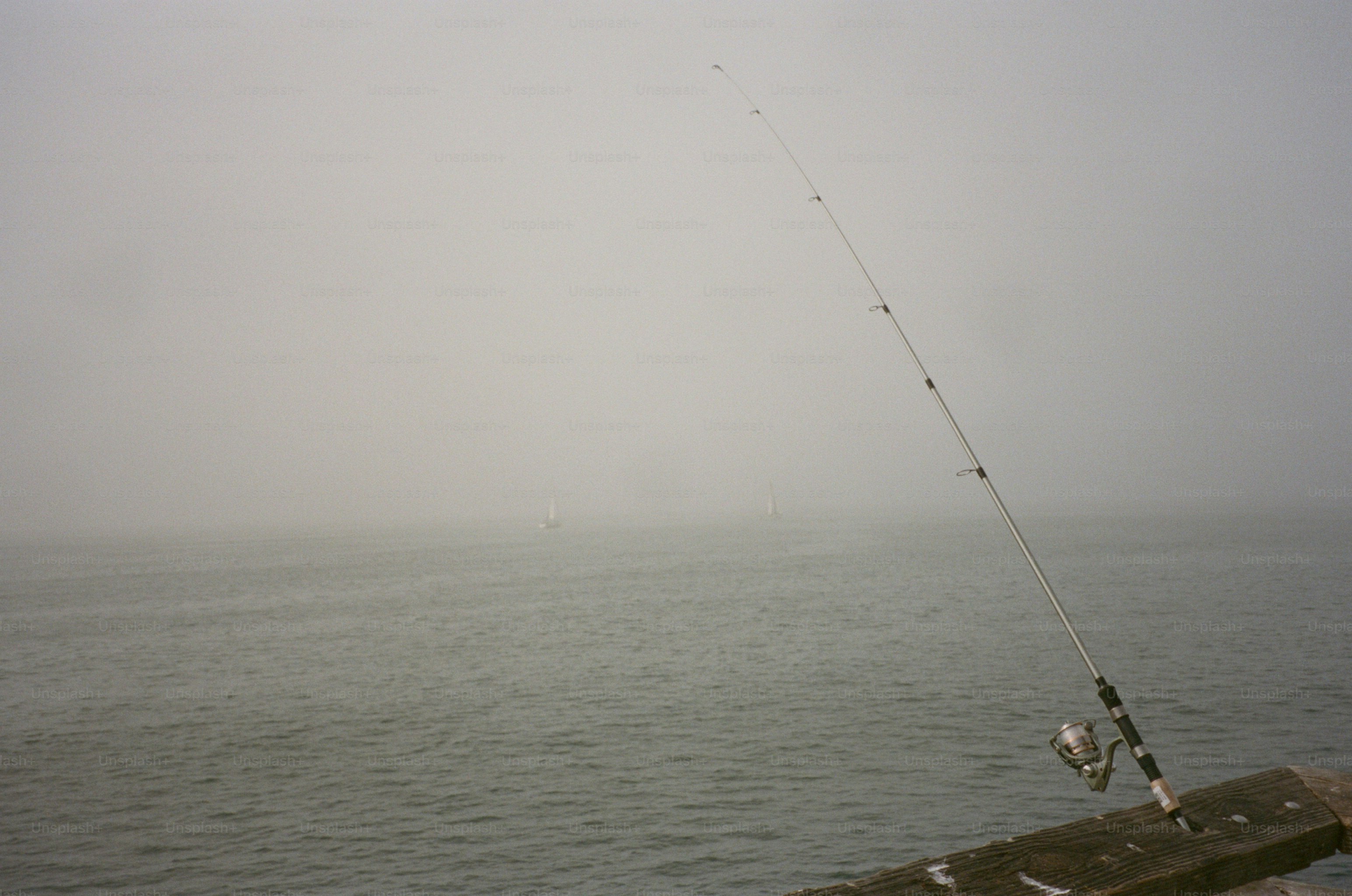 Una caña de pescar en un muelle de madera con vistas a un mar tranquilo en una densa niebla