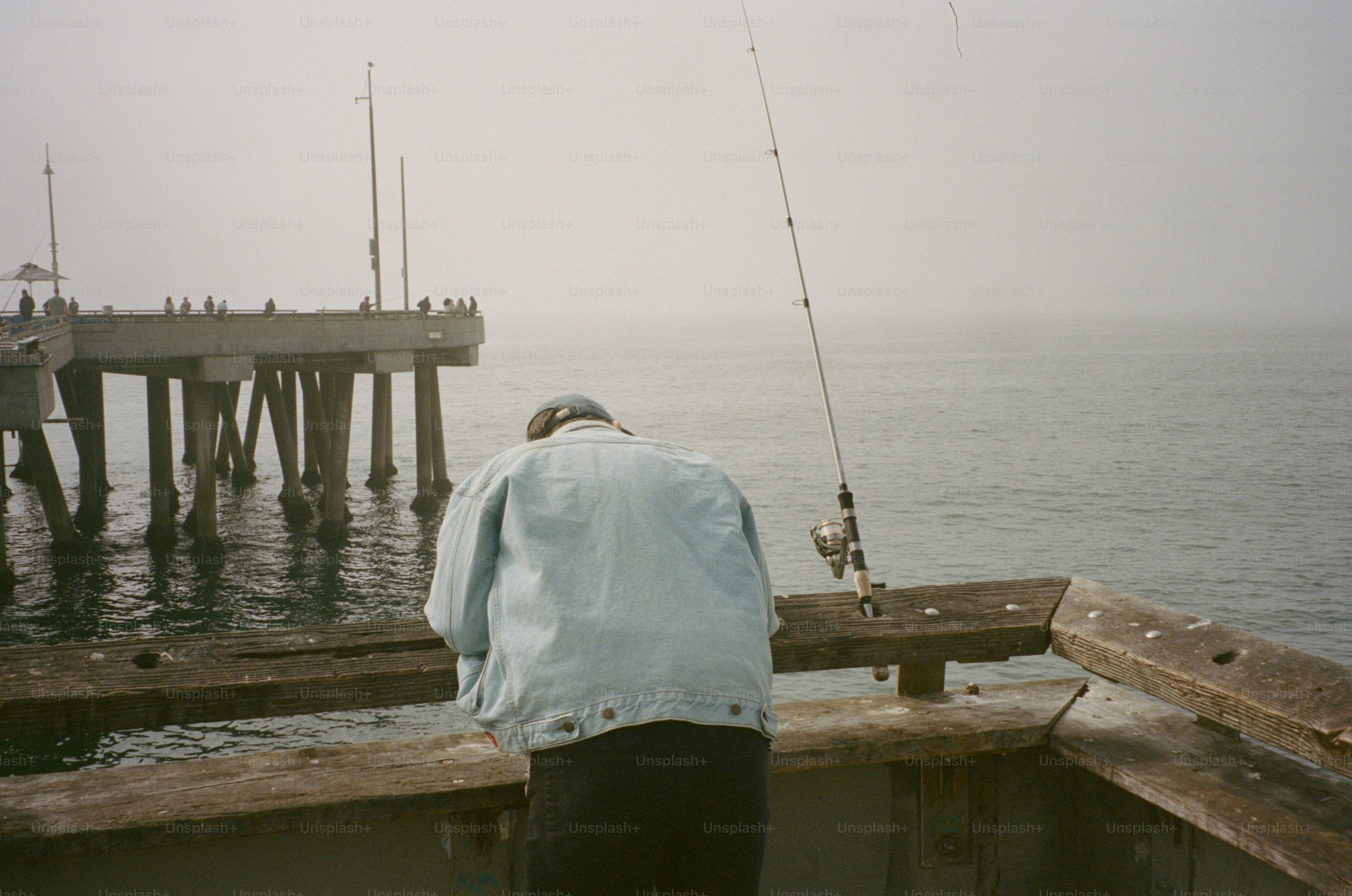 Una persona con chaqueta vaquera pescando en un muelle de madera desgastada en Los Ángeles