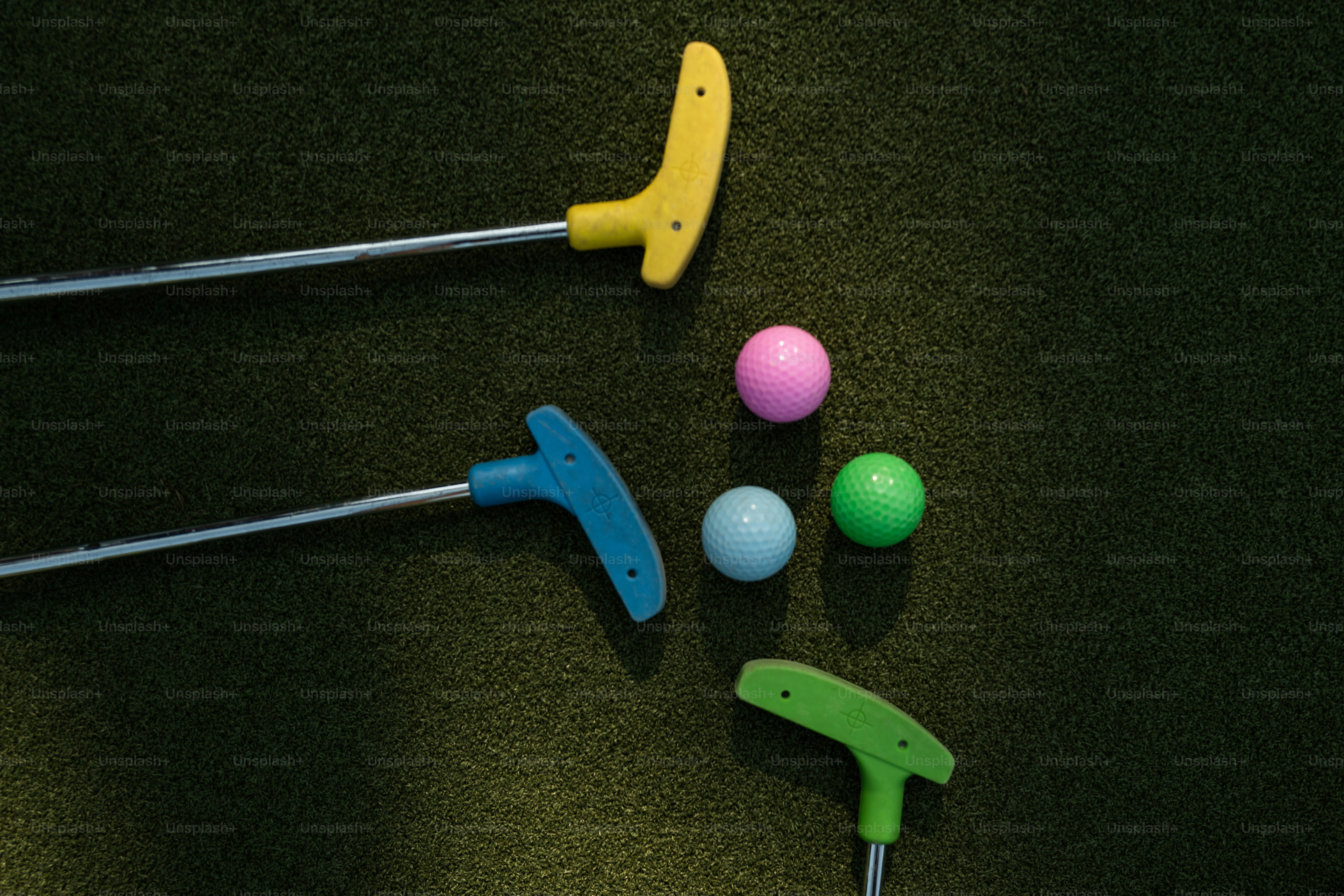 Drei bunte Golfbälle und drei Putter auf einer grünen Kunstrasenfläche
