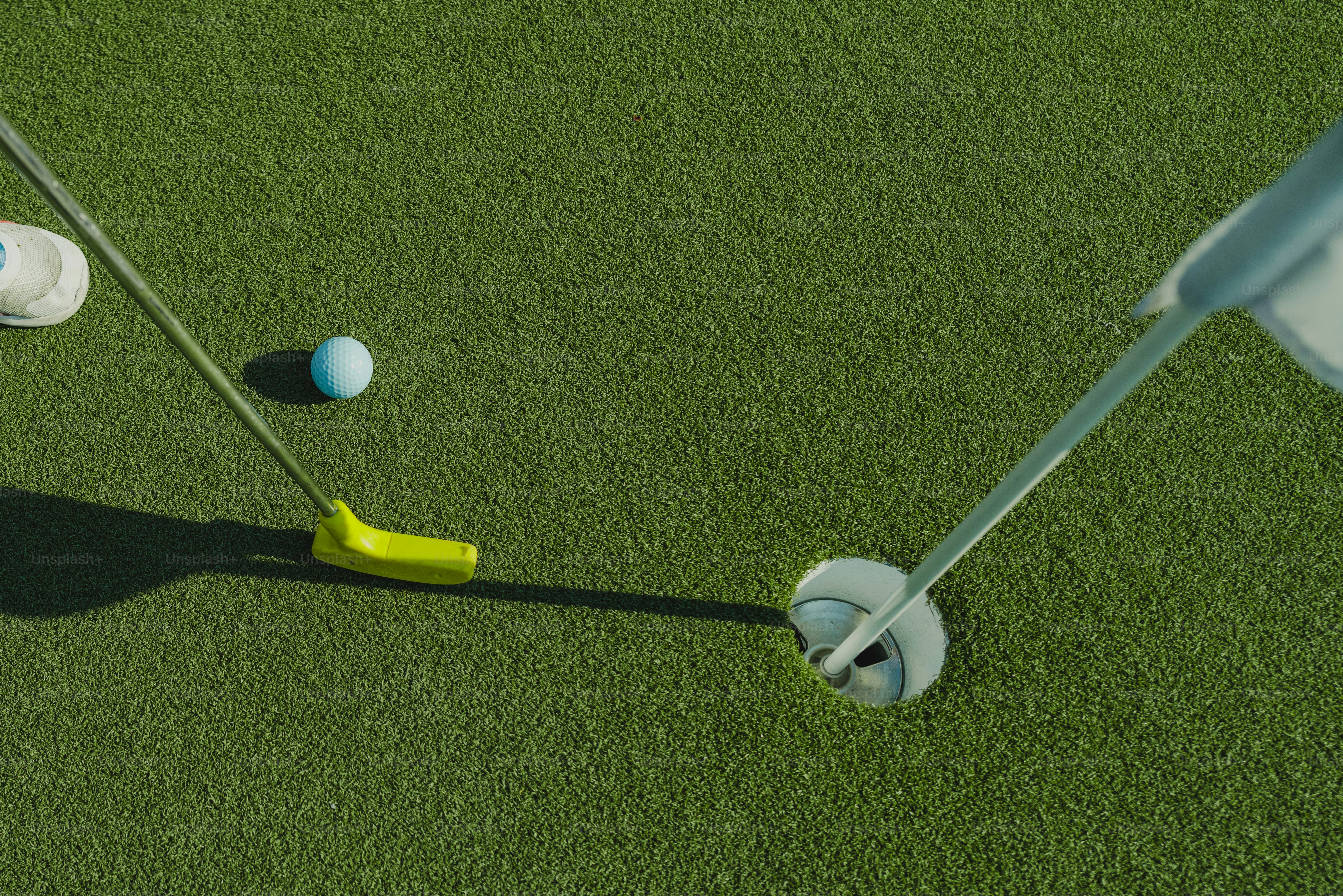 Ein gelber Putter und ein weißer Golfball auf einer grünen Puttingfläche