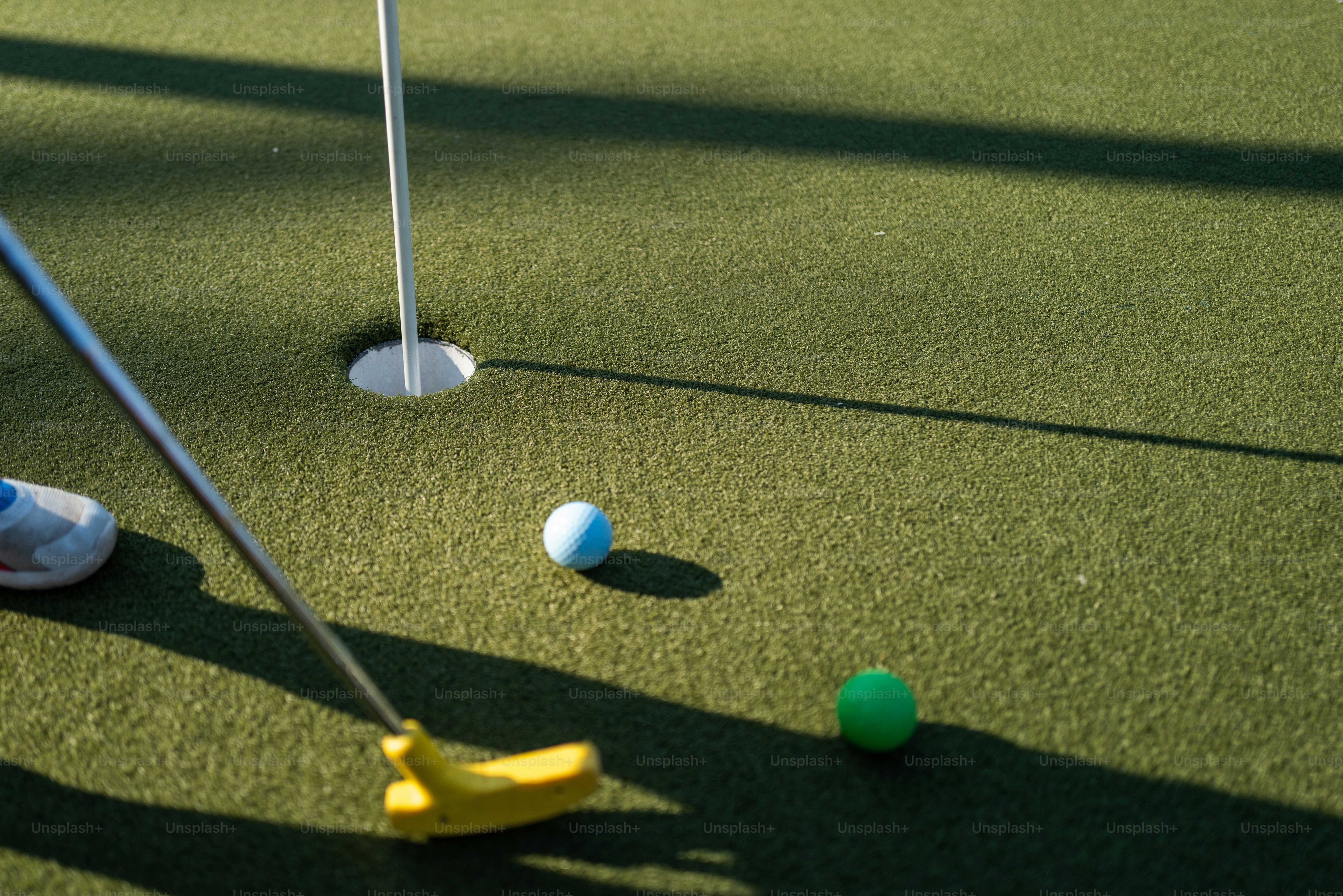 Ein gelber Putter und zwei Golfbälle auf einer grünen Puttingfläche
