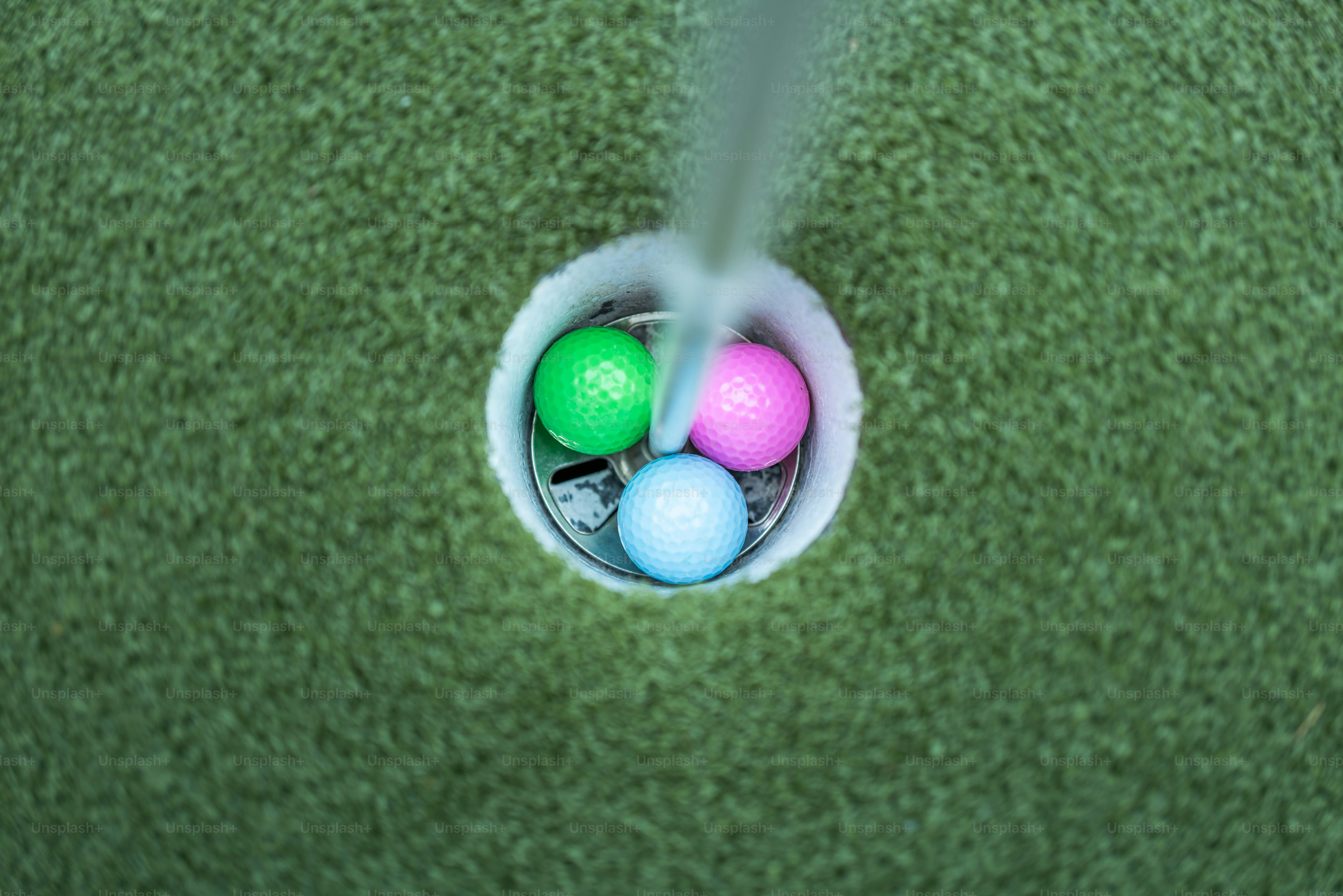 Drei bunte Golfbälle innerhalb eines Lochs auf einem Grün setzen das Putten auf
