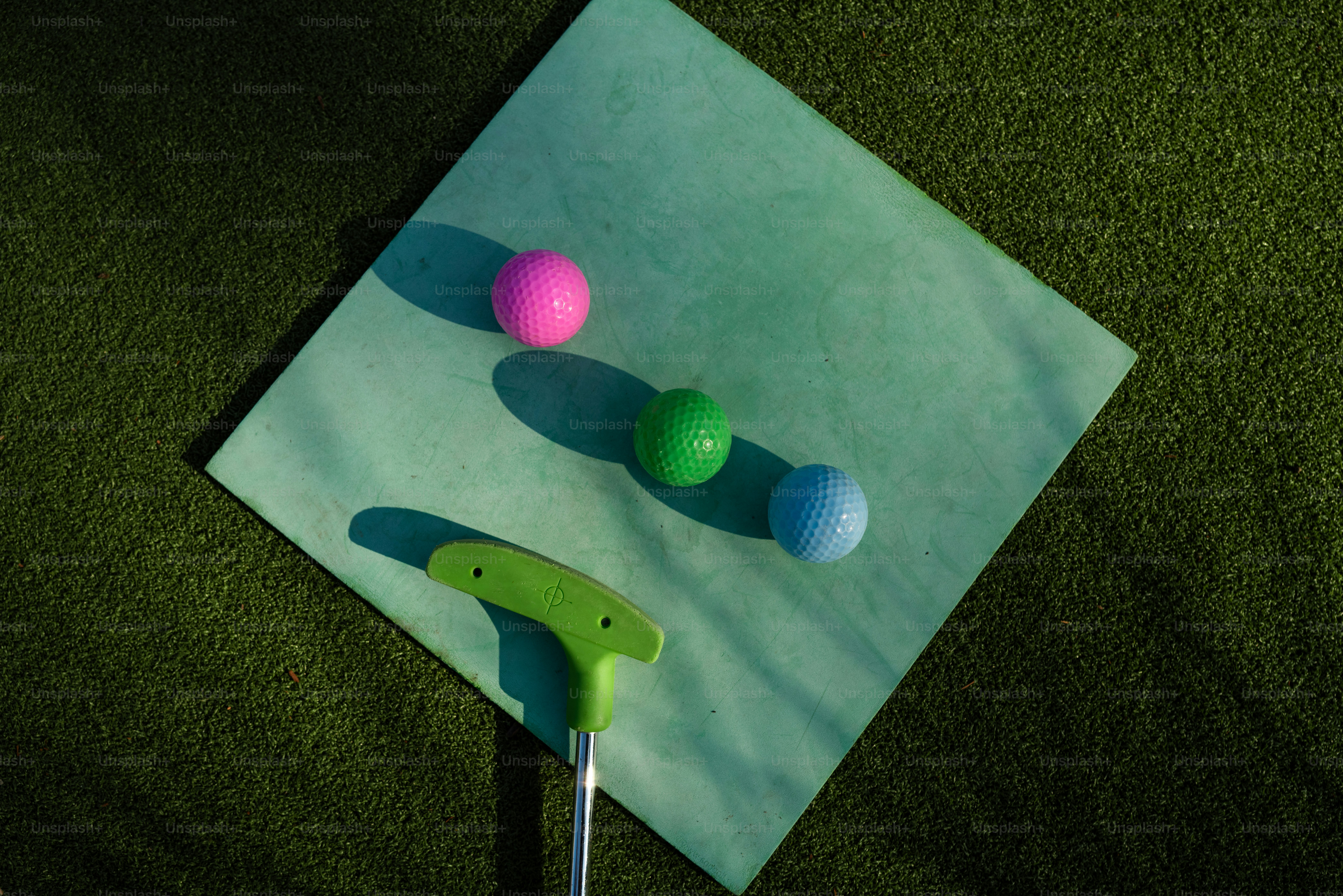 Drei bunte Golfbälle und ein Putter auf einer grünen Matte