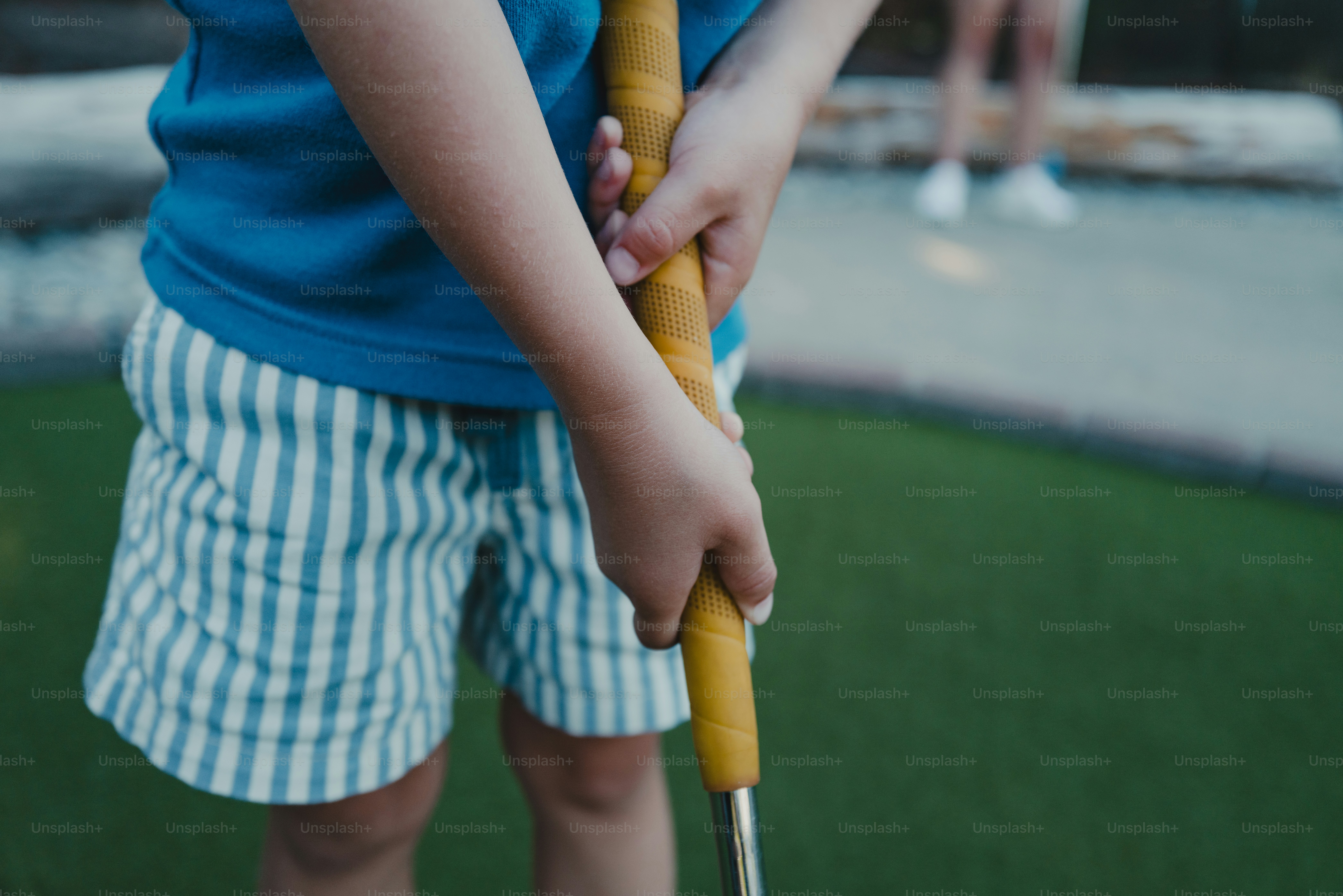 Eine Person in einem blauen Hemd und gestreiften Shorts hält einen gelben Golfschläger