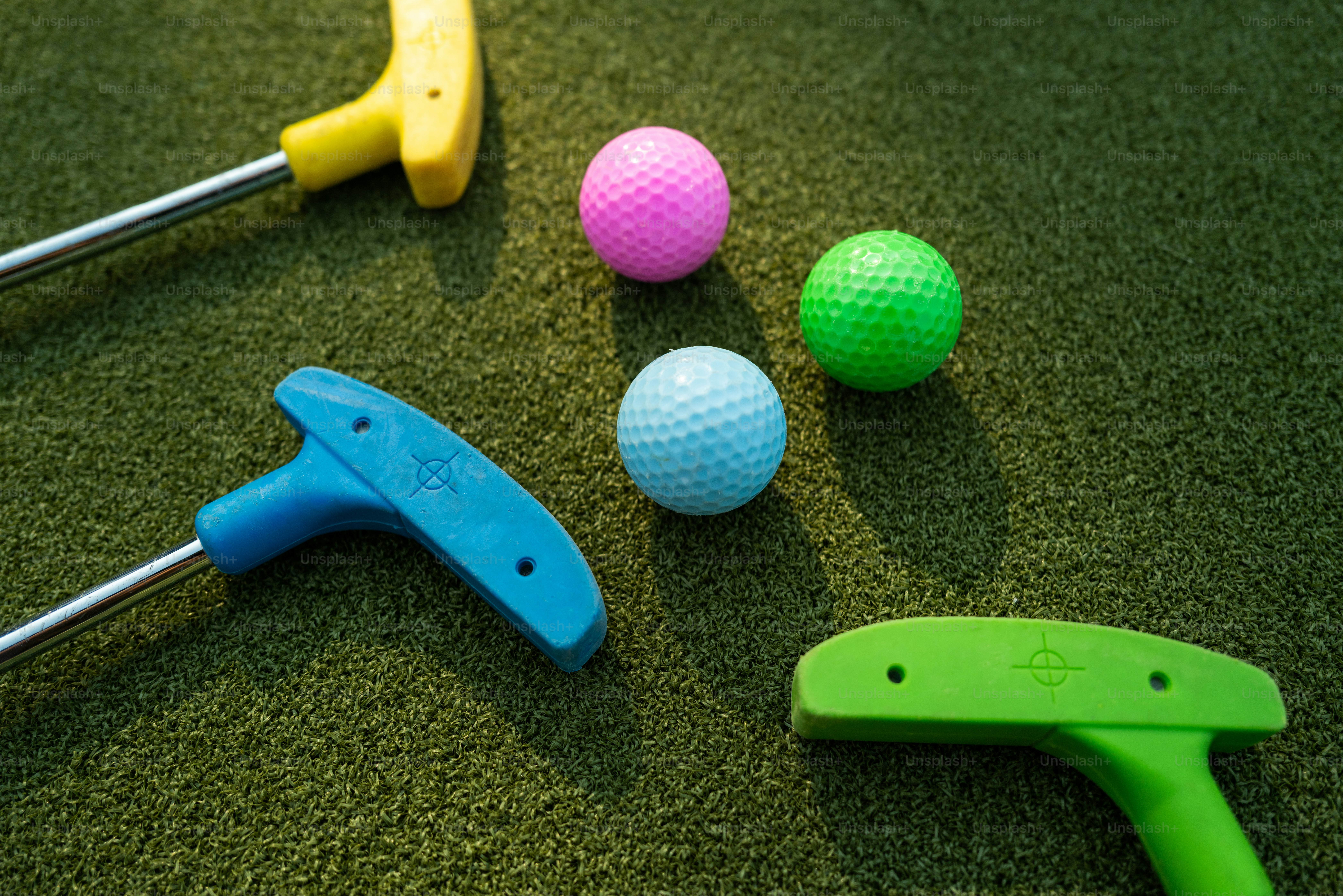 Drei bunte Golfbälle und drei Putter auf einer grünen Kunstrasenfläche