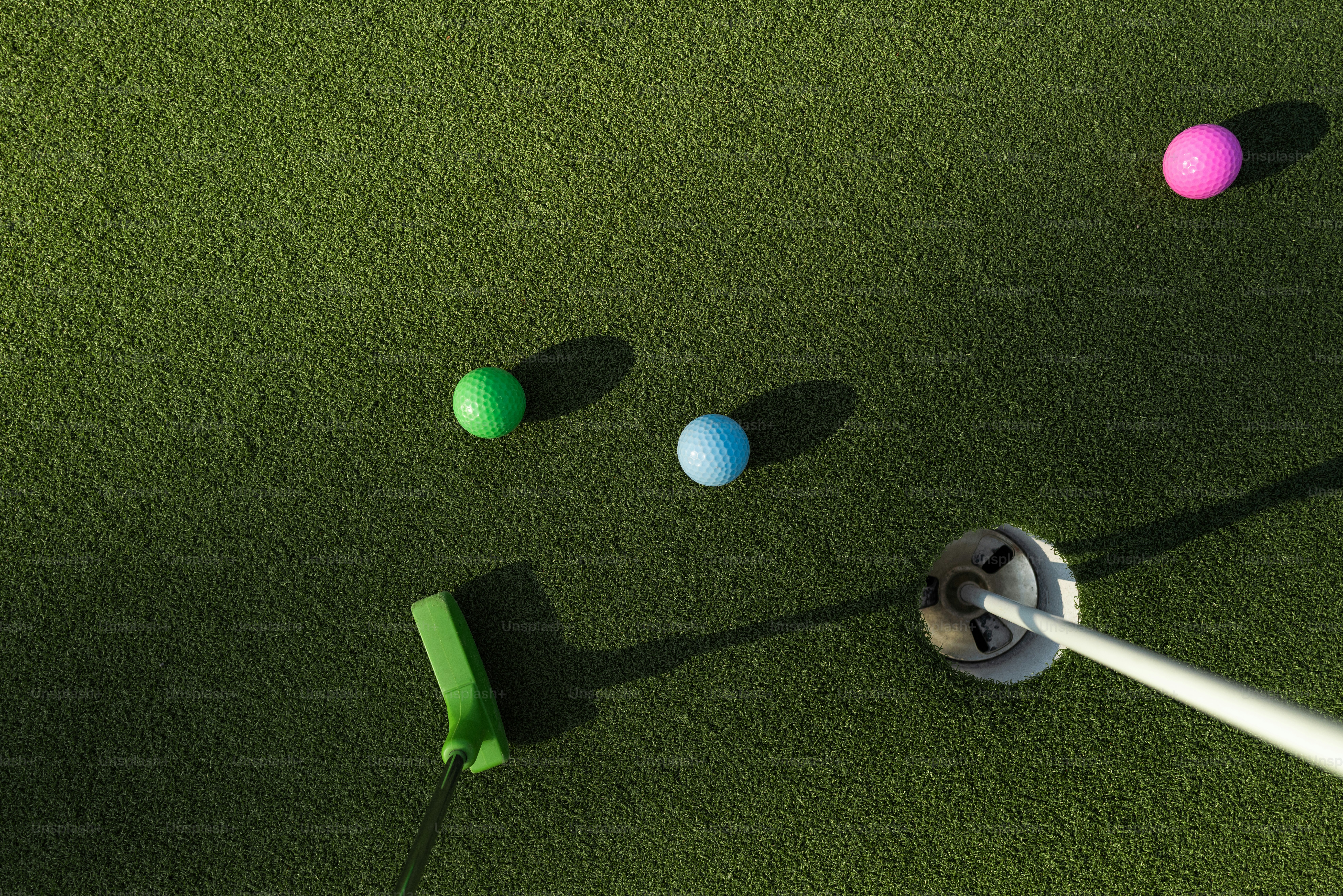 Ein Grünputter, drei bunte Golfbälle und ein Loch auf einem Puttinggrün