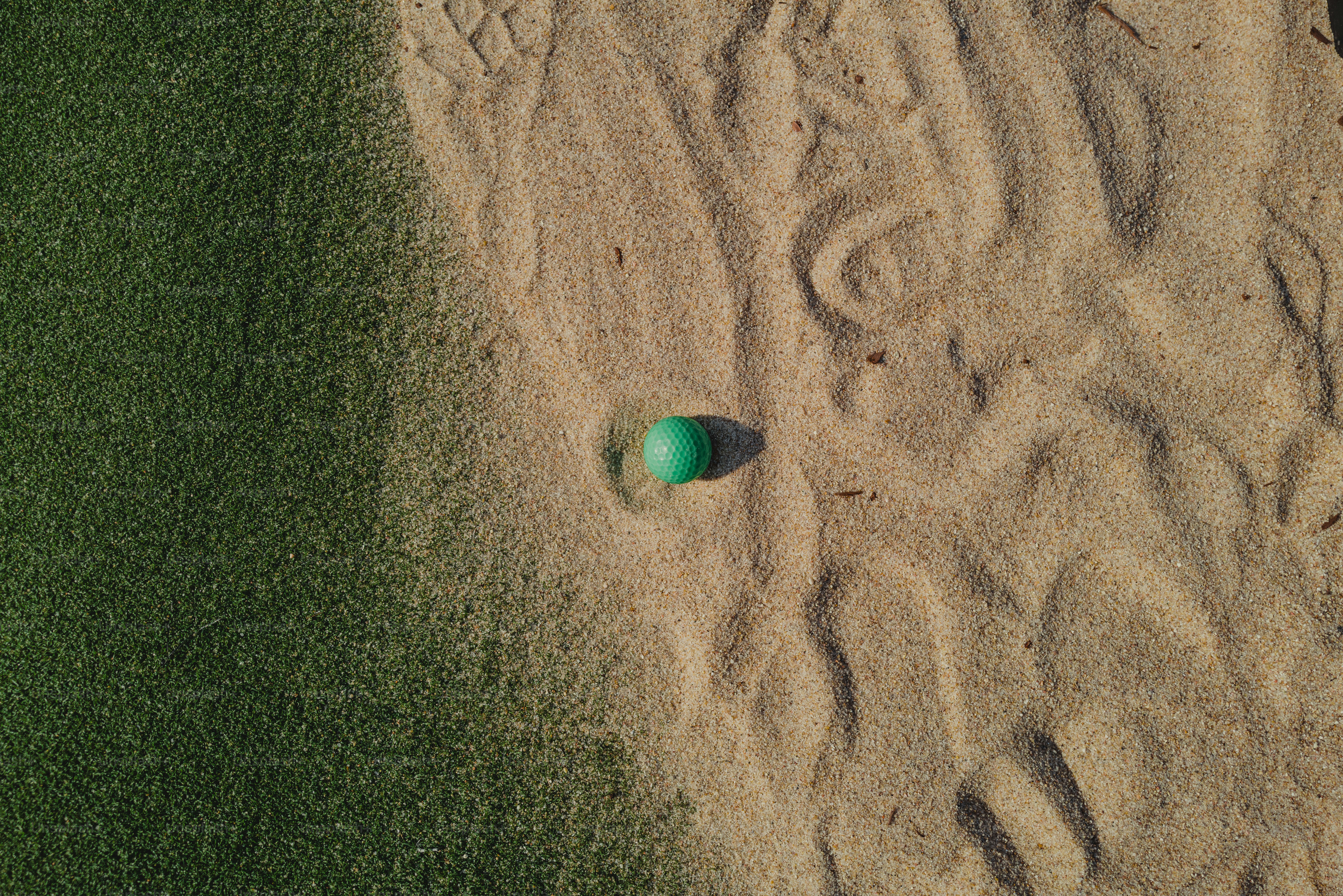 Ein grüner Golfball, der in einem Sandbunker neben grünem Rasen ruht