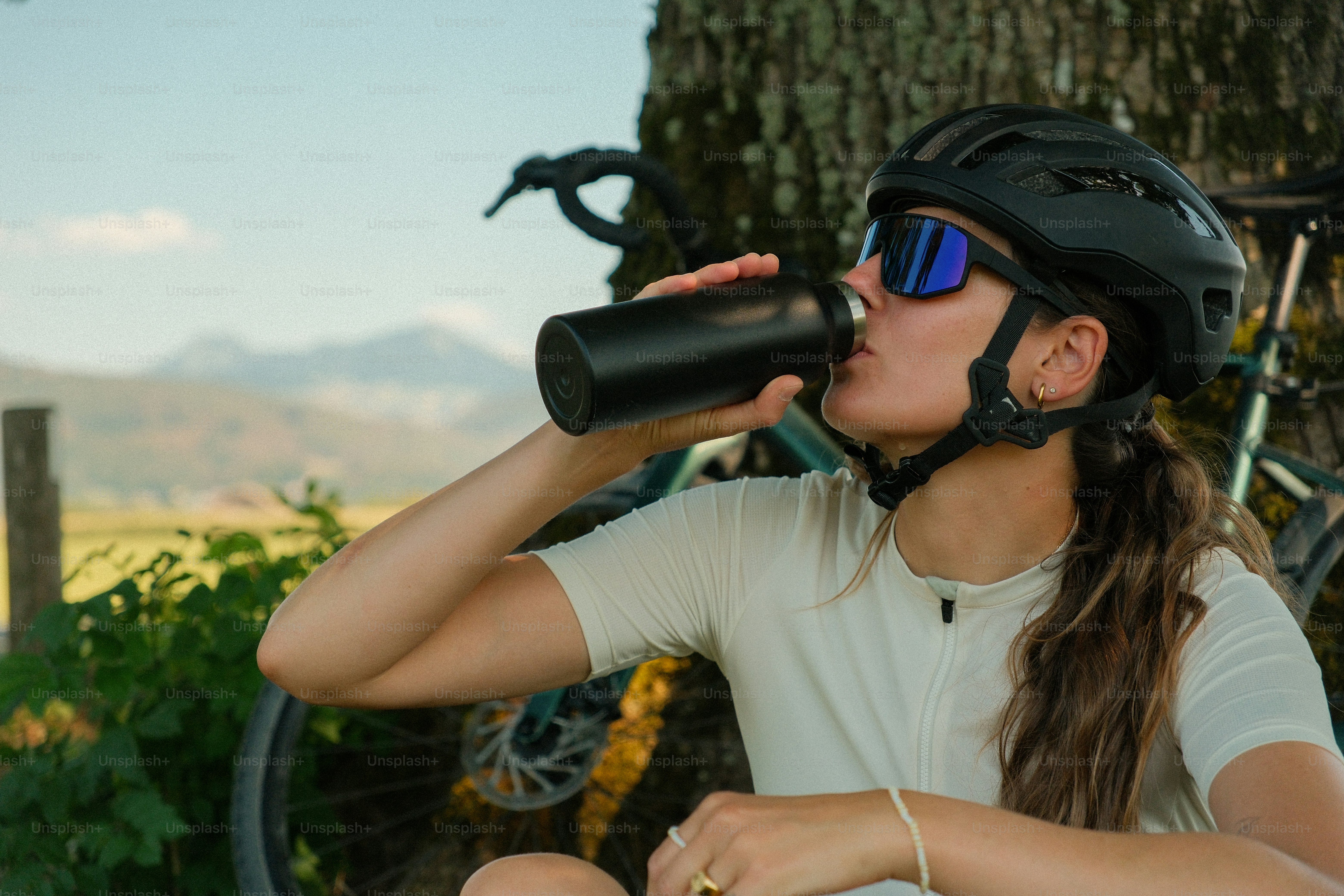 Un ciclista con elmetto e occhiali da sole che beve da una bottiglia nera all'aperto