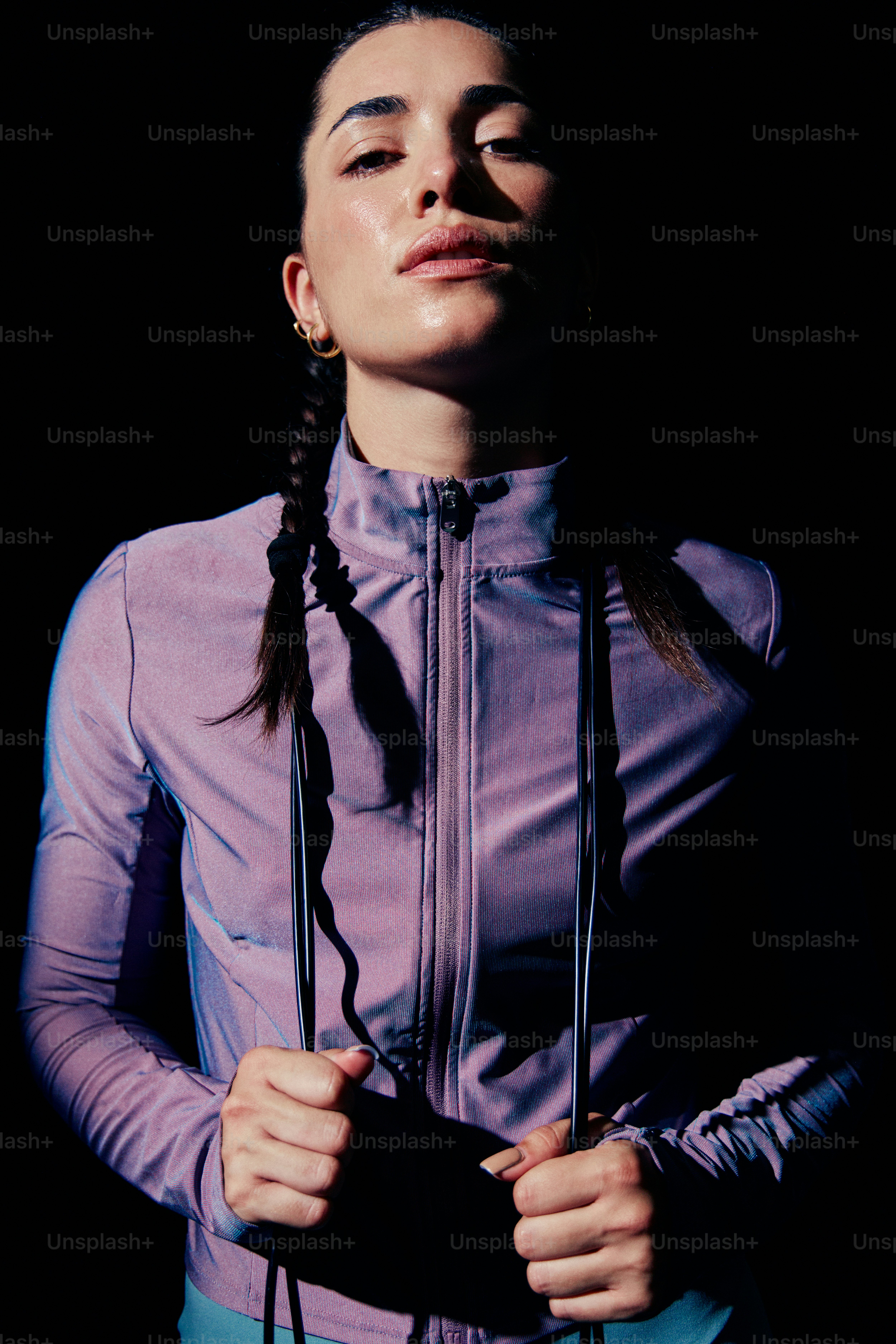 A woman in a purple zip-up jacket holding a jump rope against black