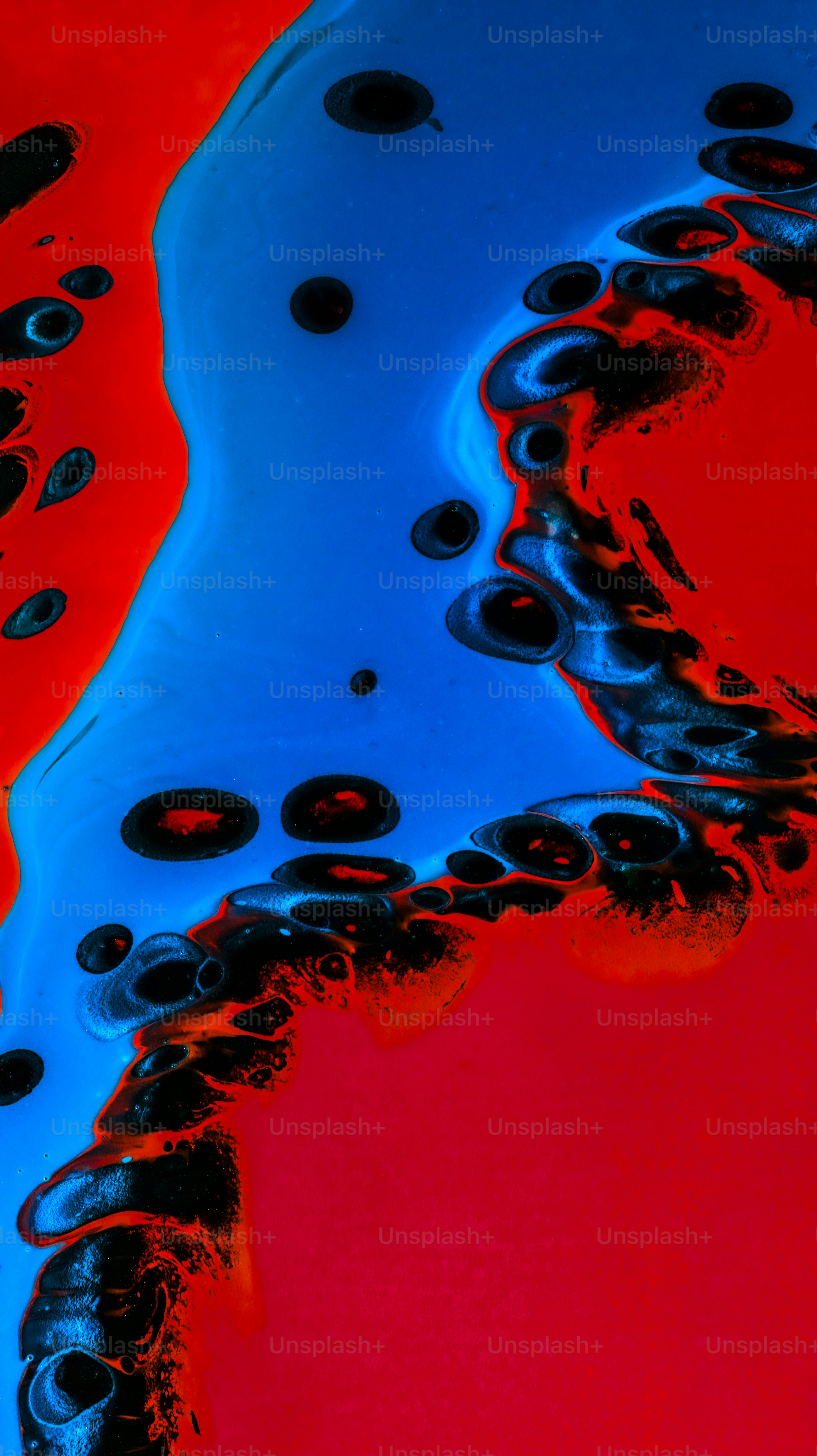 Vibrant red and blue liquid paint swirling with black circular cells