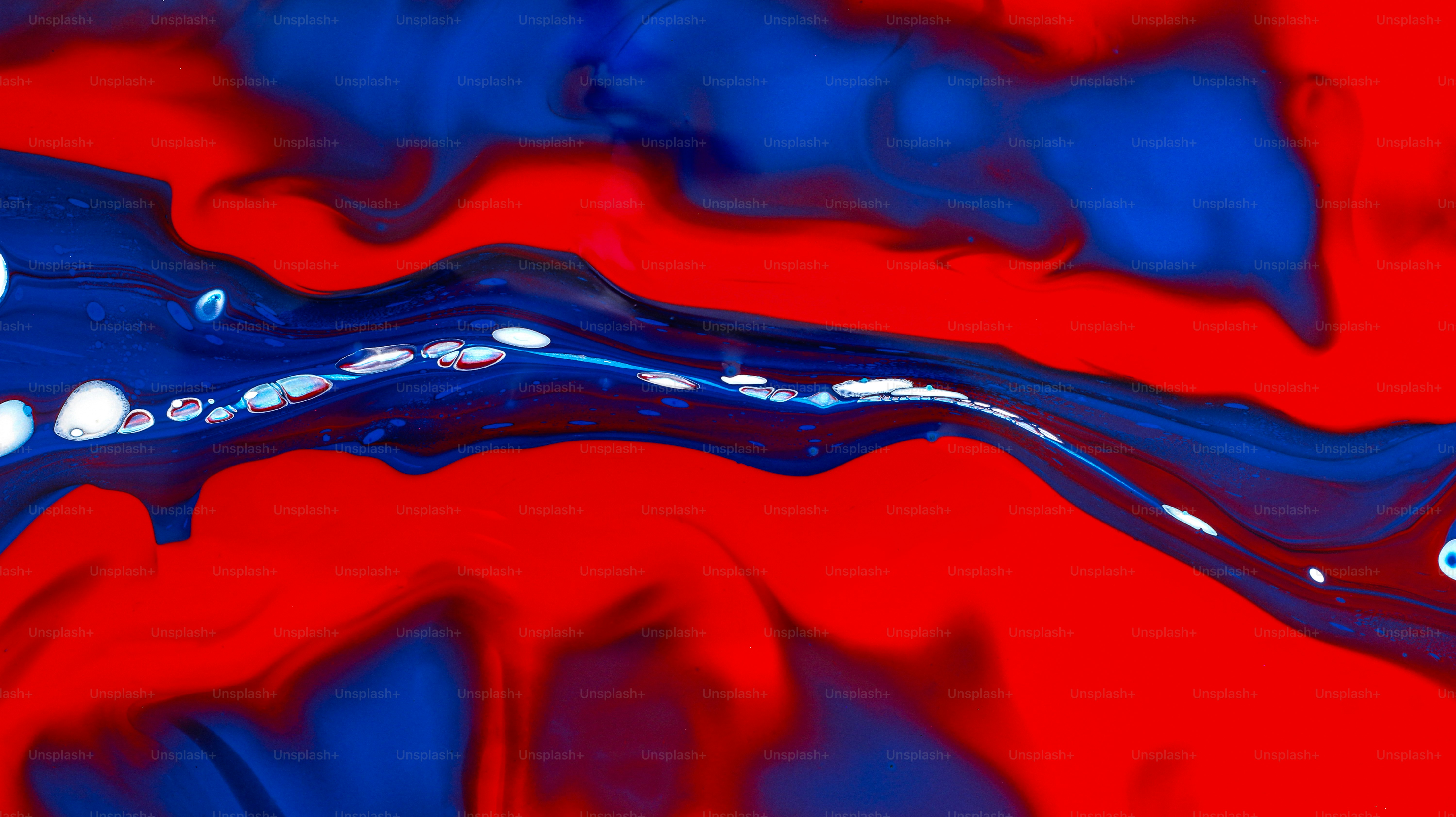 Swirling patterns of vibrant red and deep blue liquid paint with white bubbles